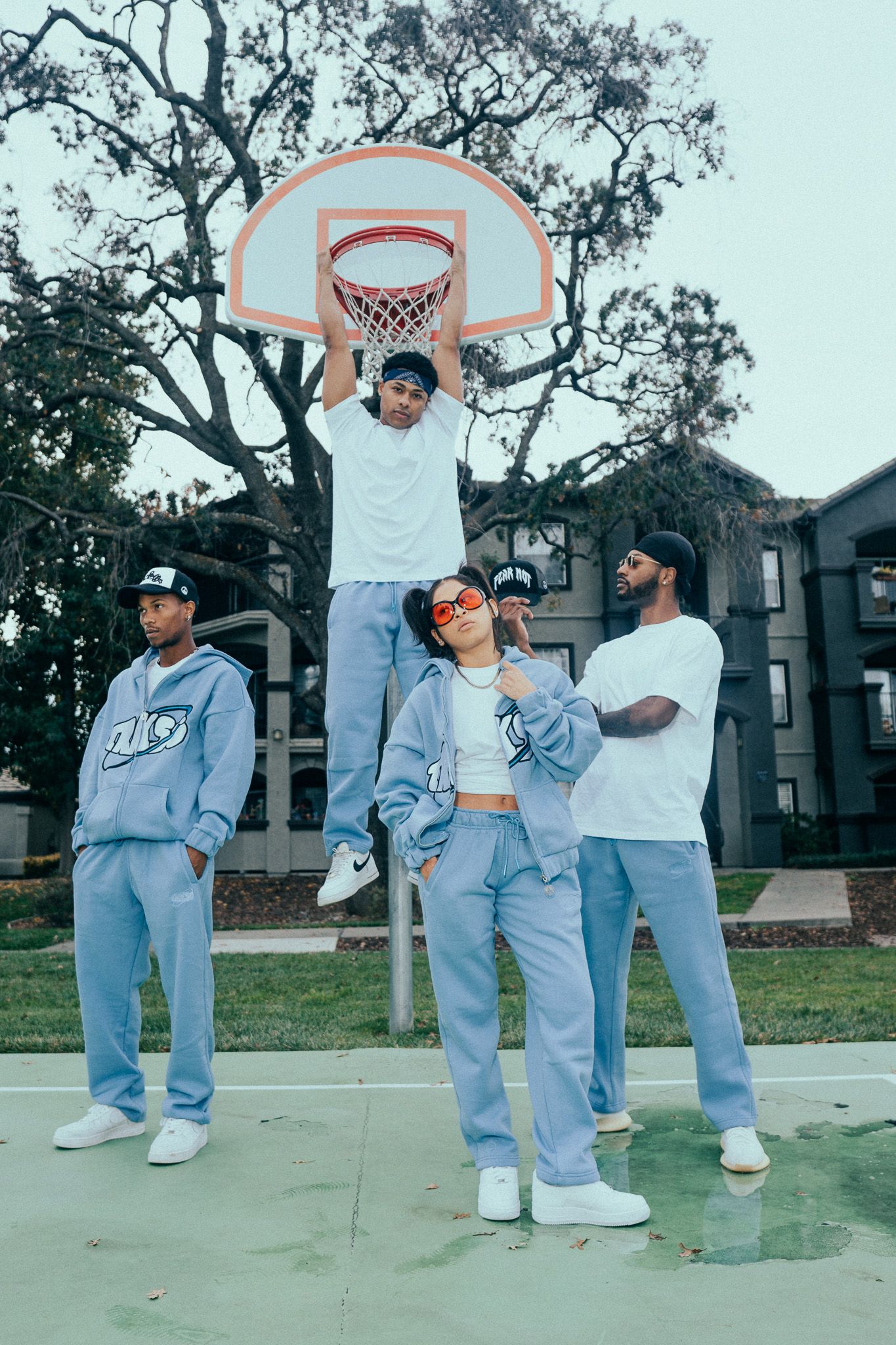 Four friends pose on an outdoor basketball court in matching blue Nike streetwear outfits near a hoop.