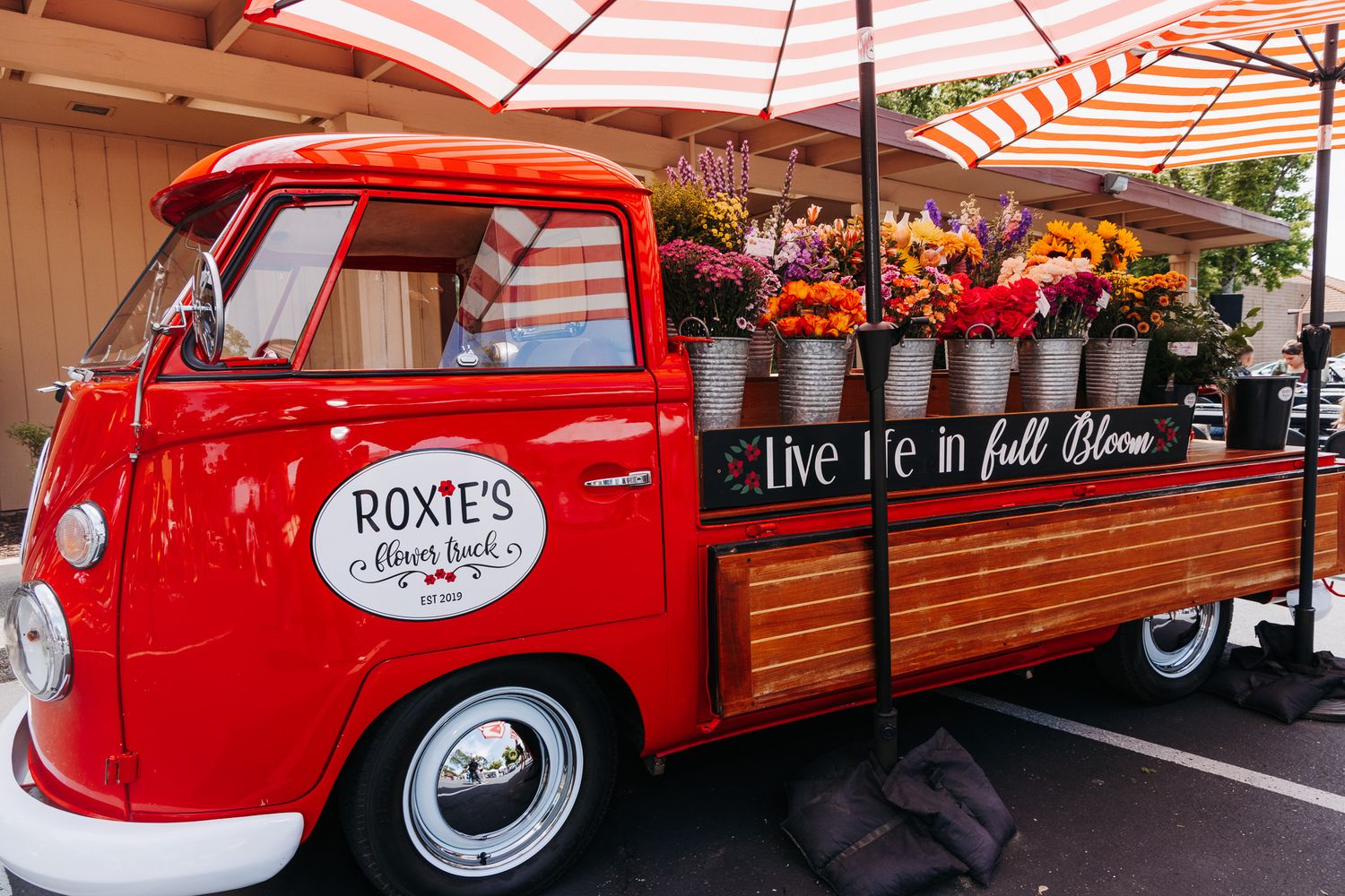Roxies flower truck, a red vintage VW bus filled with colorful fall blooms at an outdoor market.