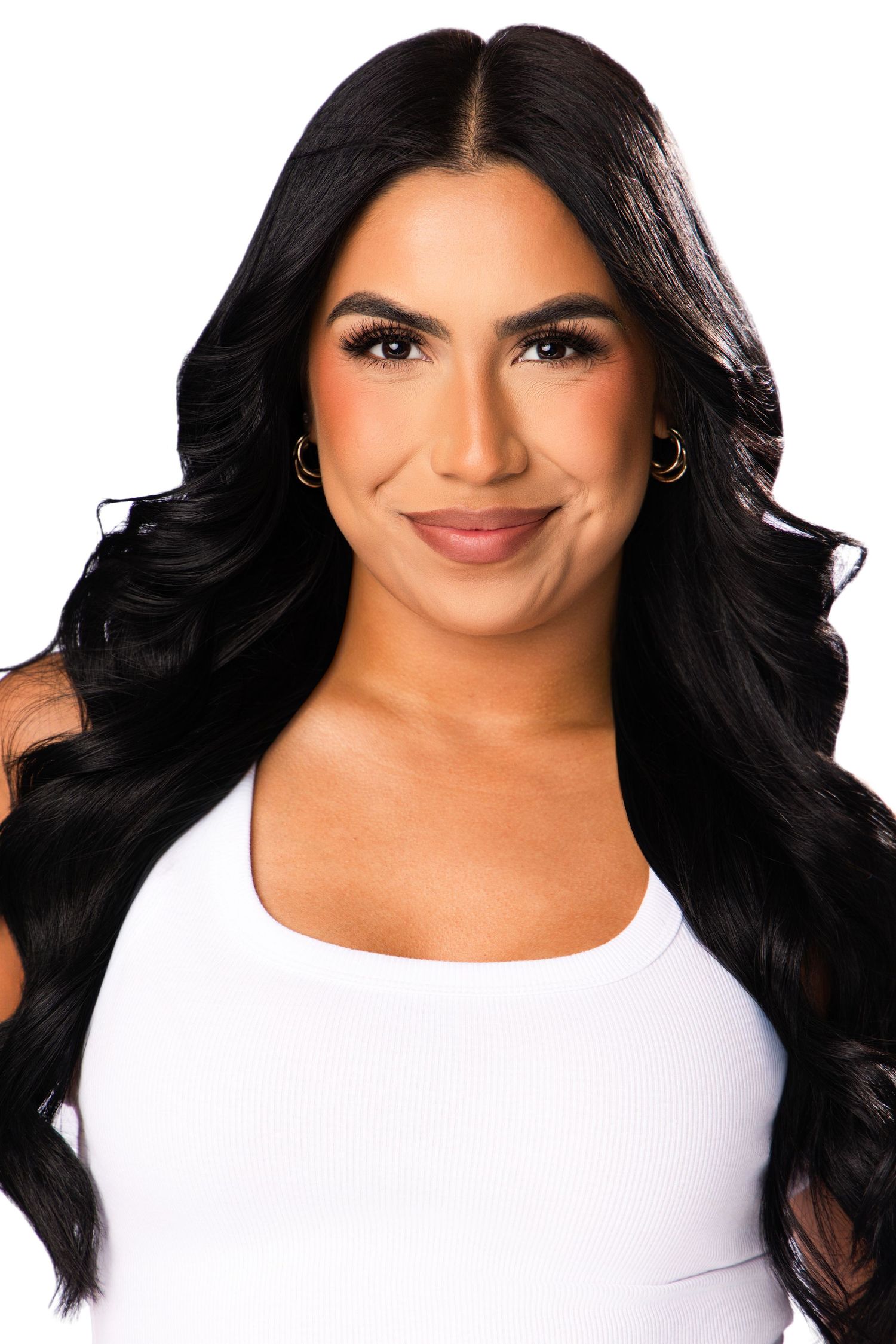 Young woman with long black wavy hair wearing a white top, smiling confidently against a white background.