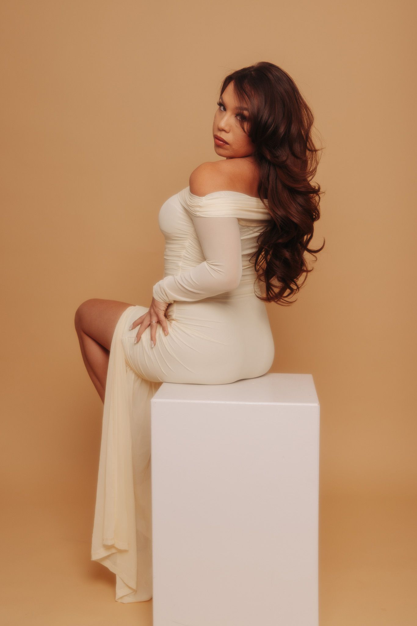 A series of artistic maternity photos showing a person in a white dress posing on a white cube against a beige backdrop.