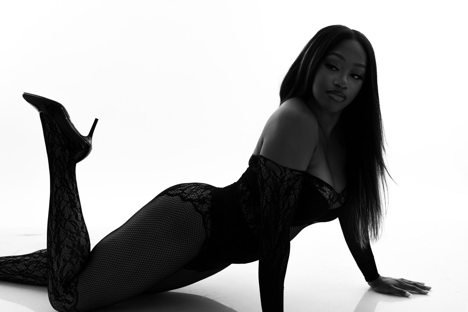 Black and white artistic portrait of a person posing on the floor in dark attire against white background.