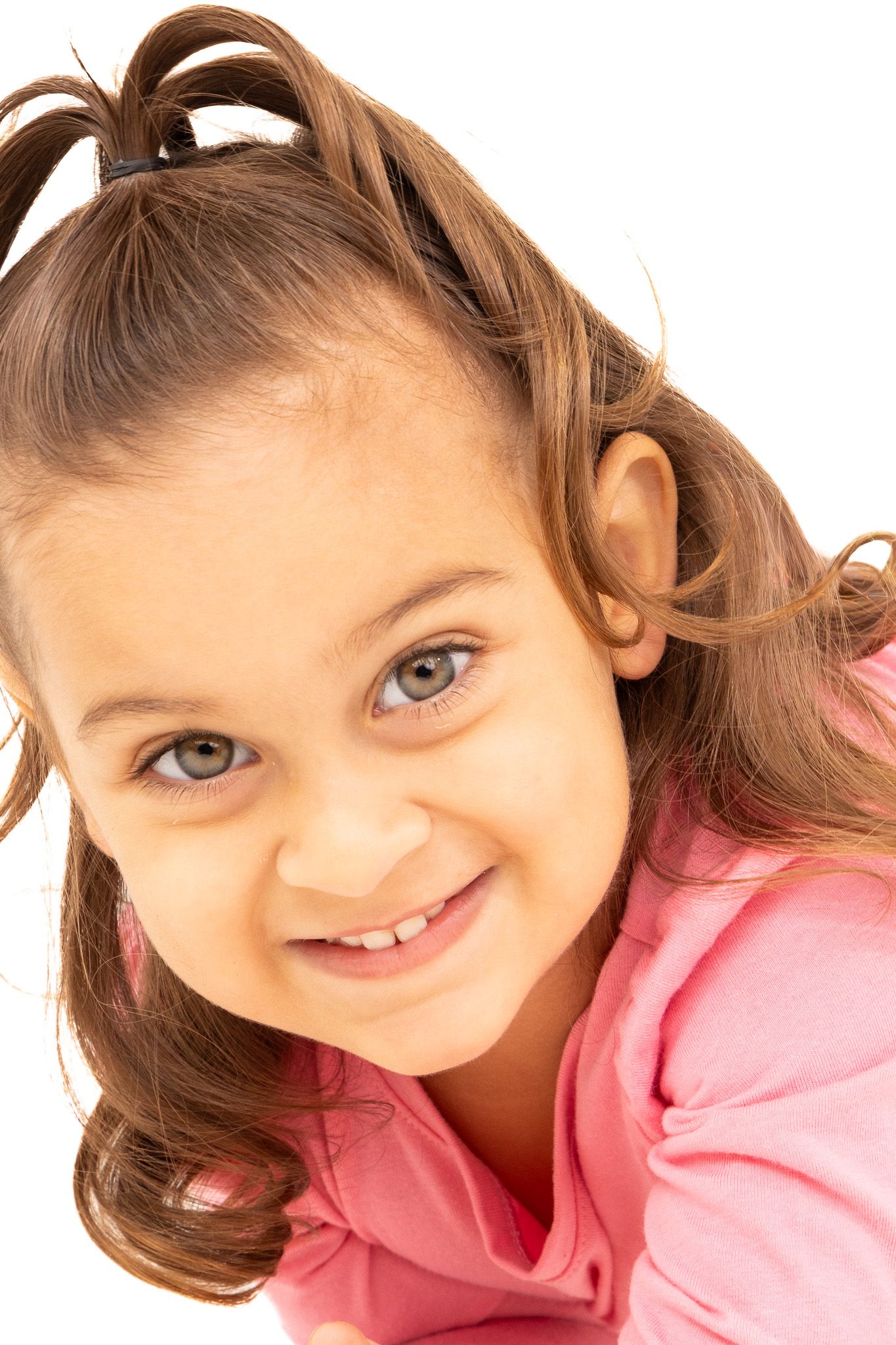 Young child in pink shirt with pigtails smiling at different angles on white background.