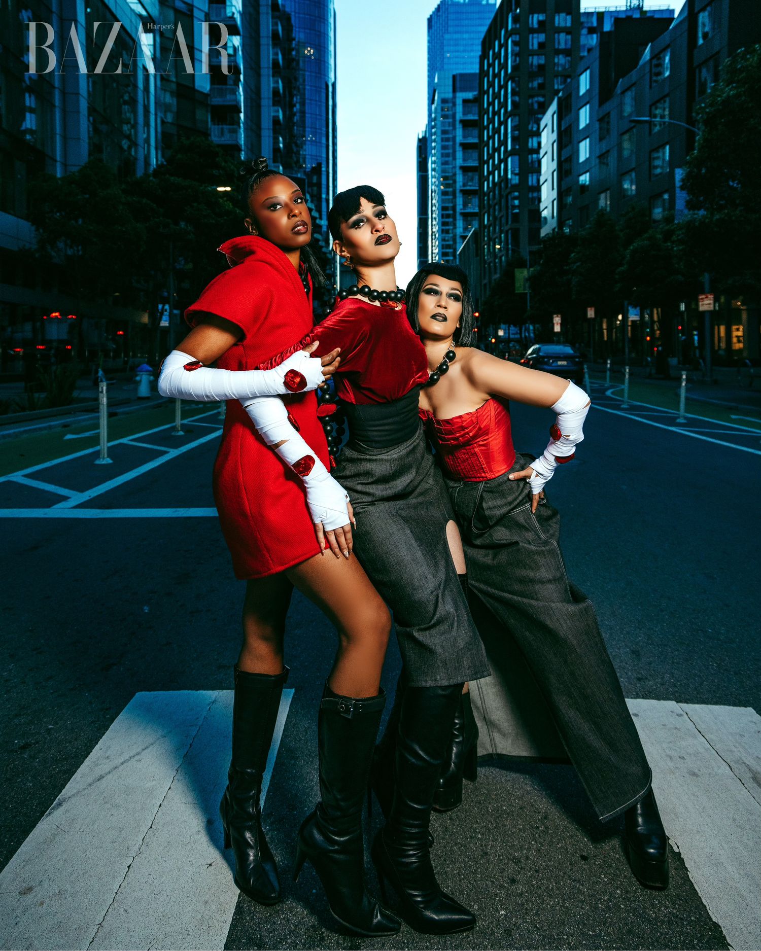 Two people pose playfully in an urban street setting wearing contrasting red and dark outfits at dusk.