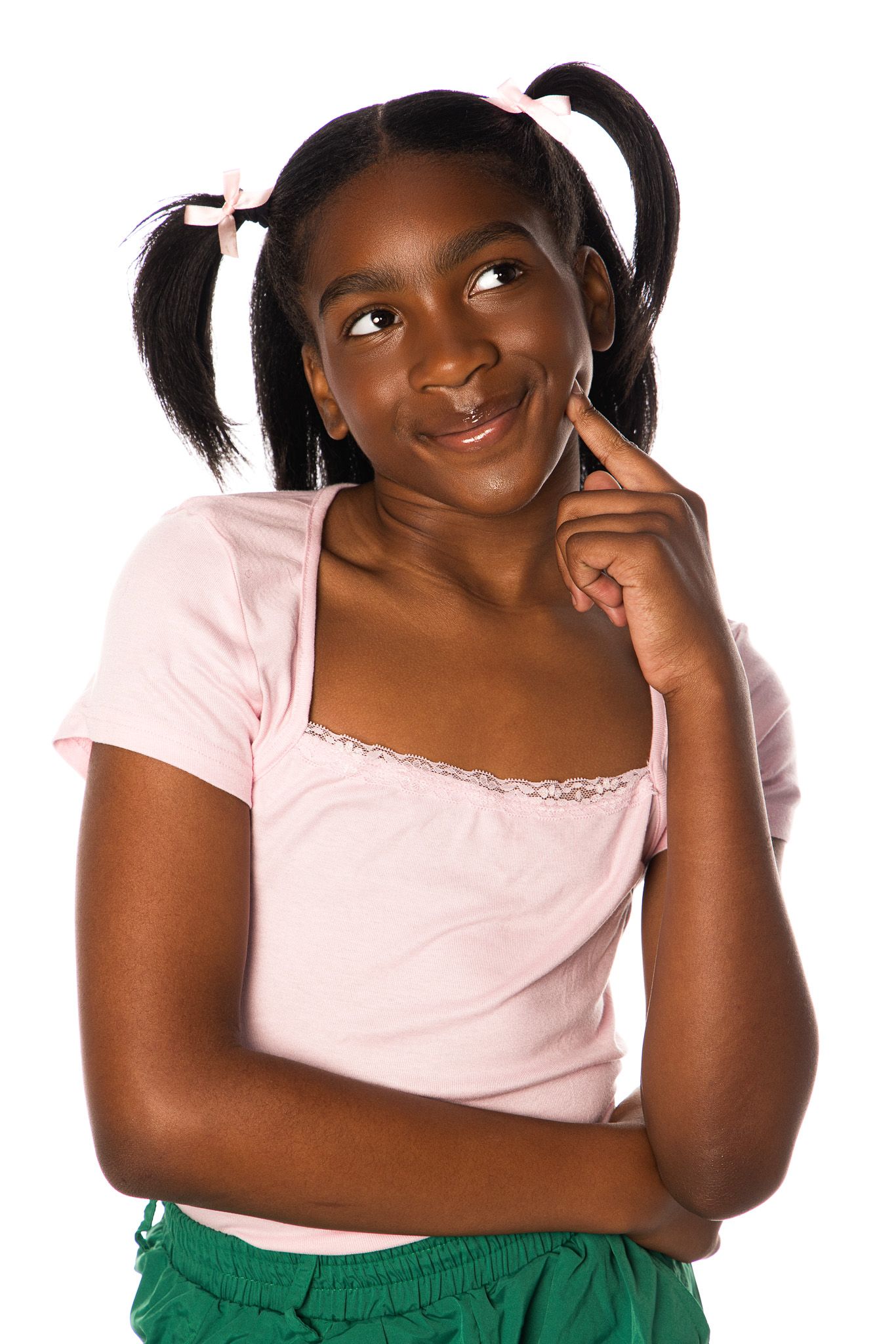 A thoughtful person wearing a pink t-shirt and green pants with pigtails poses with finger on chin against white background.