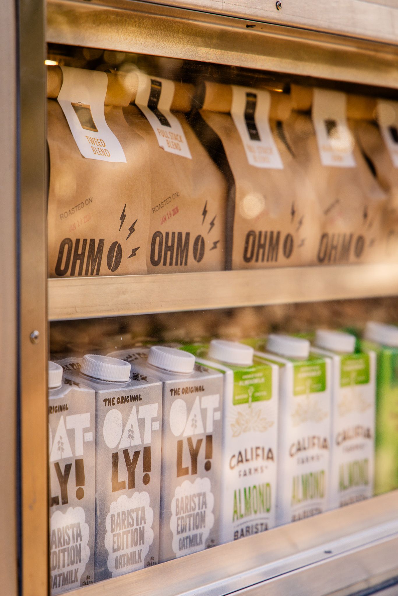 Glass storage containers with various oat milk and alternative dairy products lined up neatly on retail shelves.