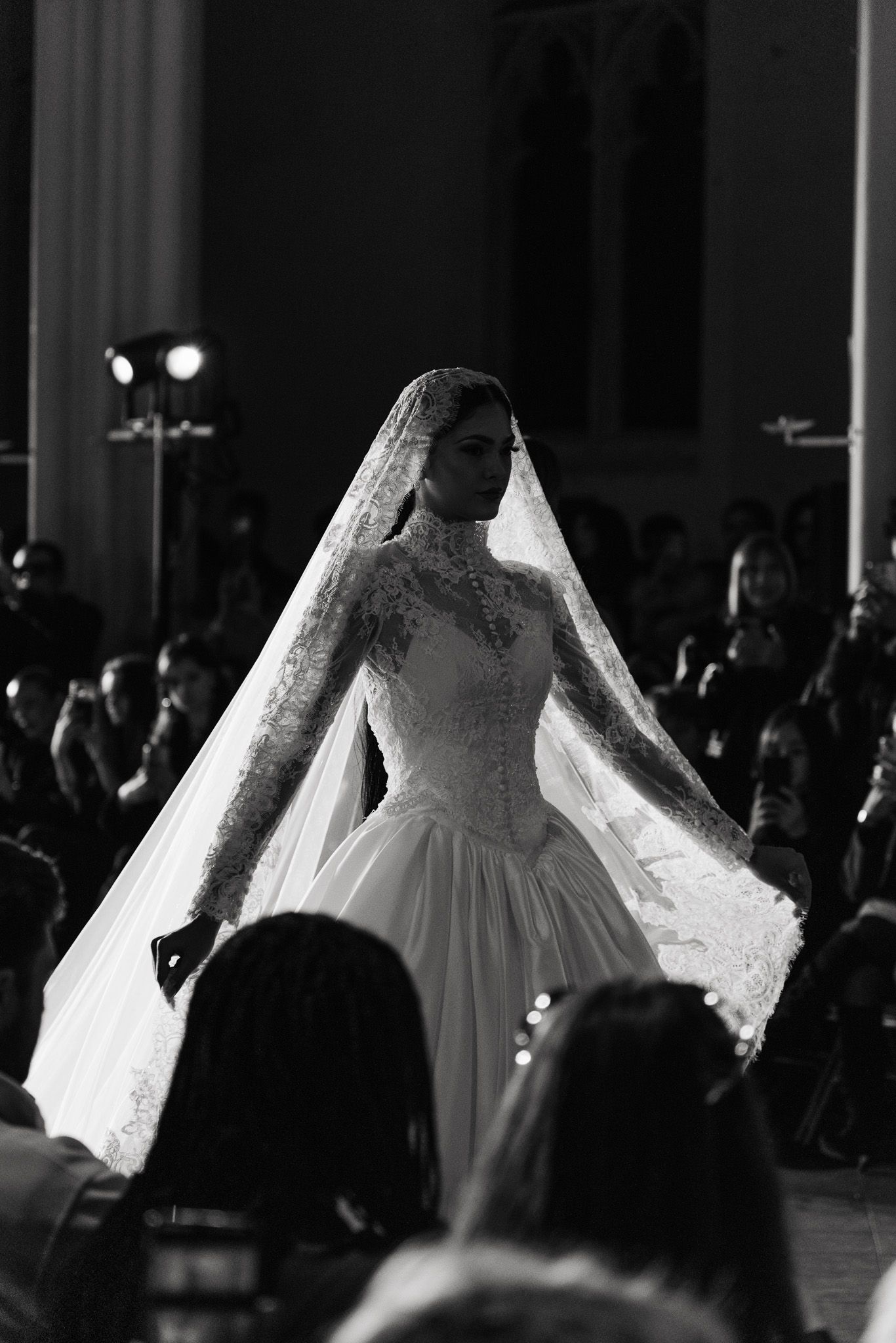 Ethereal wedding dresses with flowing silhouettes displayed on a dimly lit runway during a bridal fashion show.