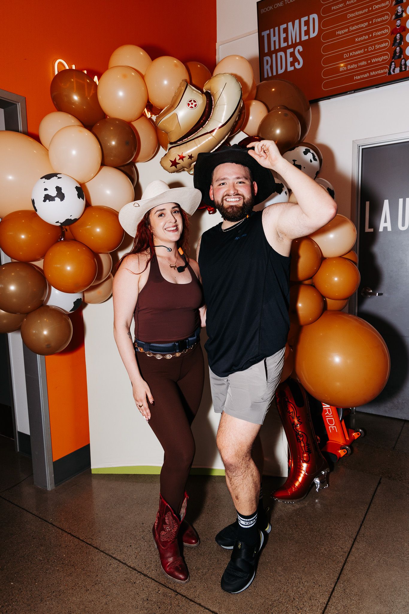 Party attendees in western-inspired outfits pose together under a festive balloon arch decoration.
