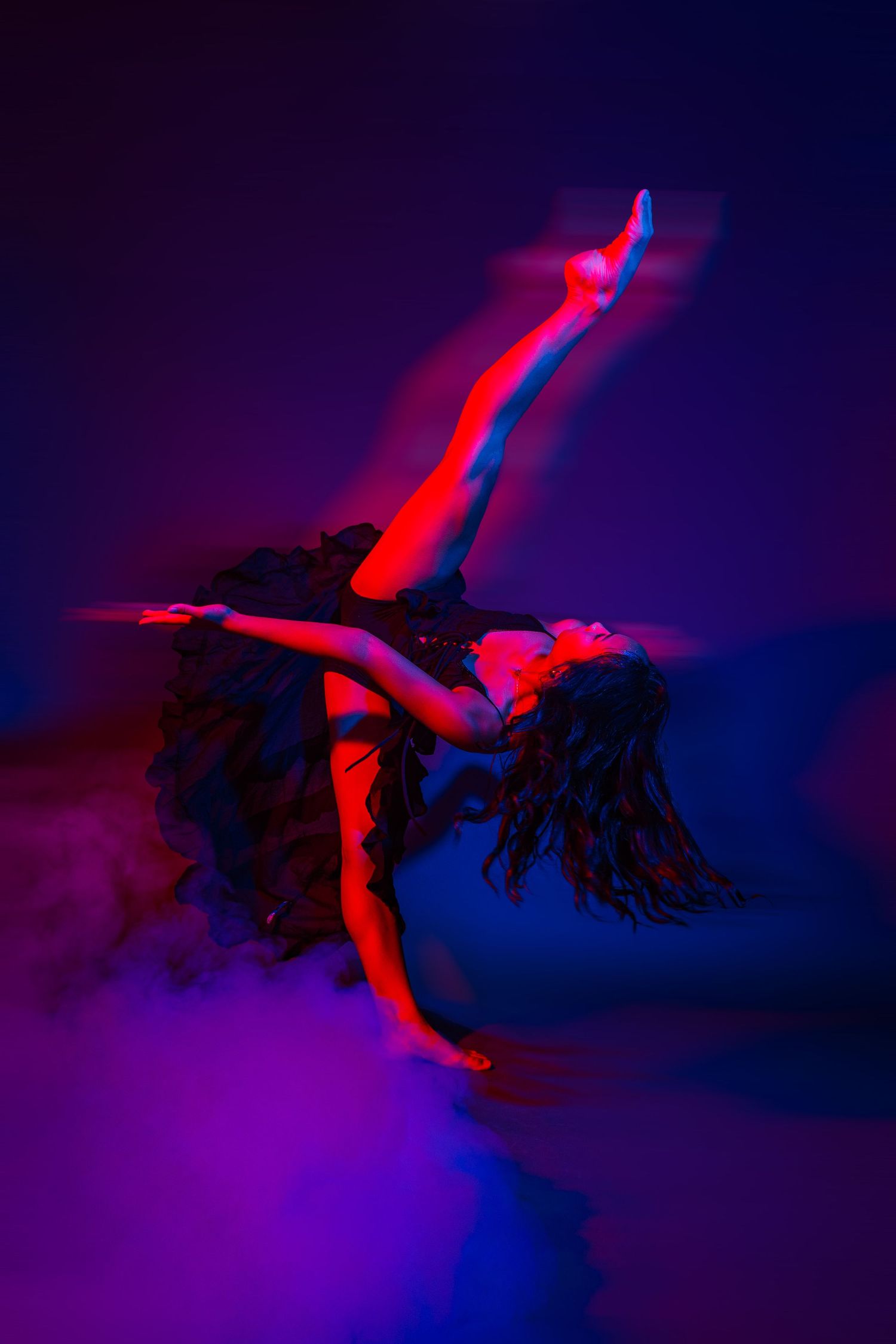 Contemporary dancer creates dynamic shapes against dark background with red and blue lighting effects.