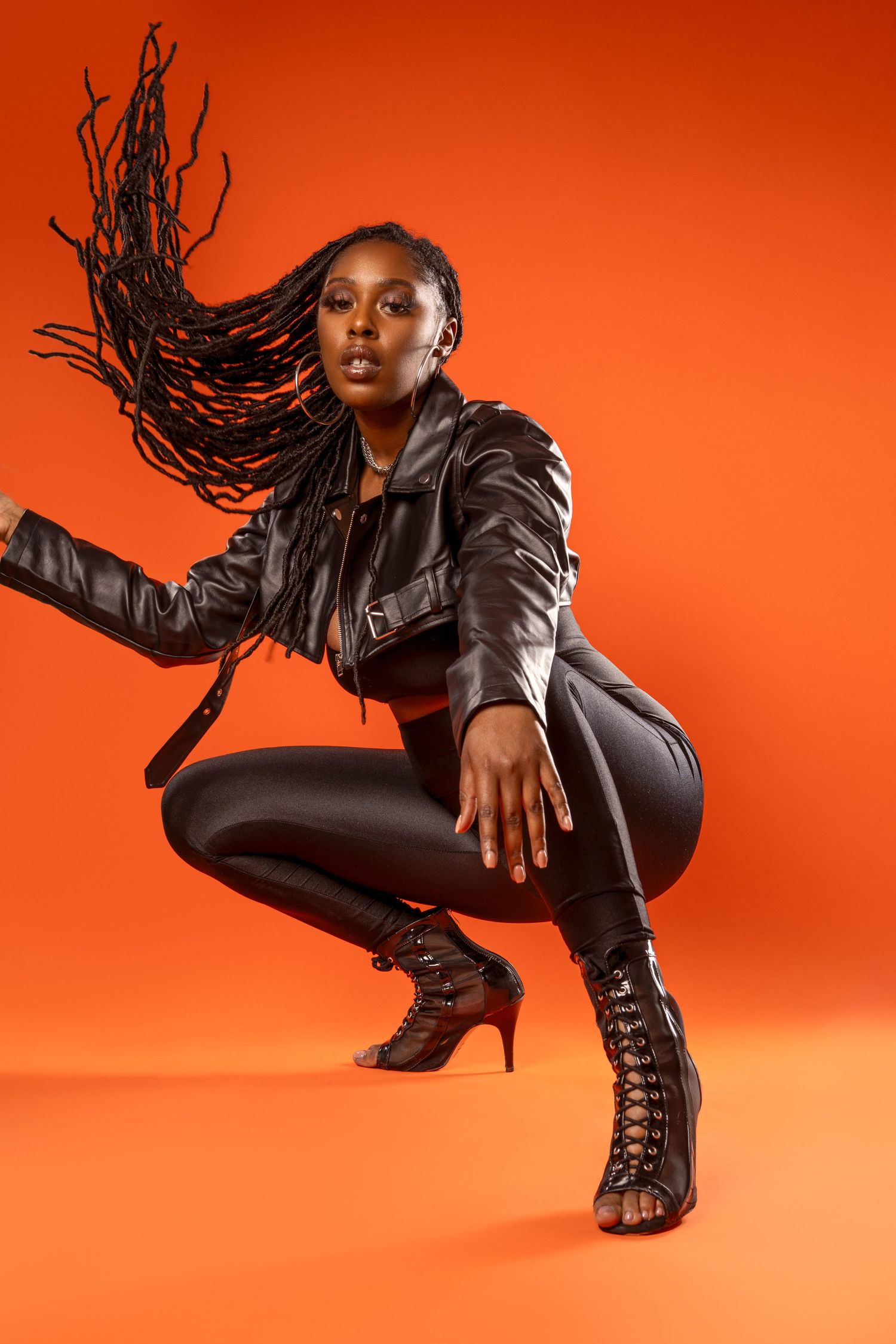 Dynamic fashion photoshoot on orange backdrop featuring model wearing black leather jacket and boots in motion poses.