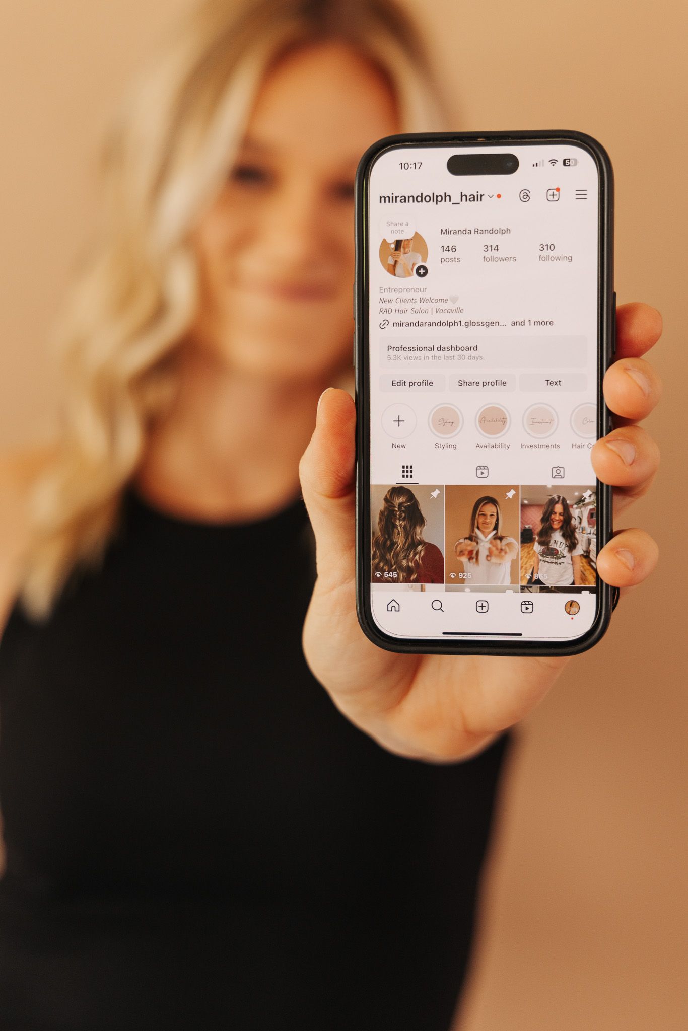 Hand holding smartphone displaying social media profile with arranged highlight story covers in warm peachy tones.