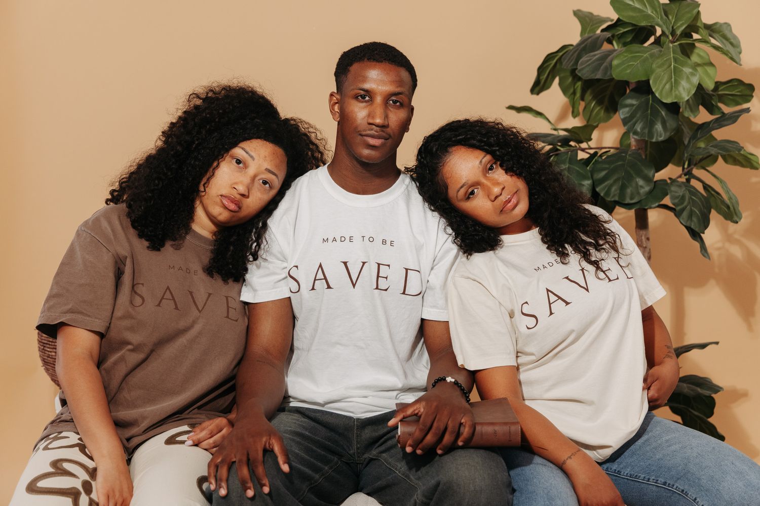 A group of friends sitting together on a couch wearing coordinated brown and white t-shirts that say SAVED.