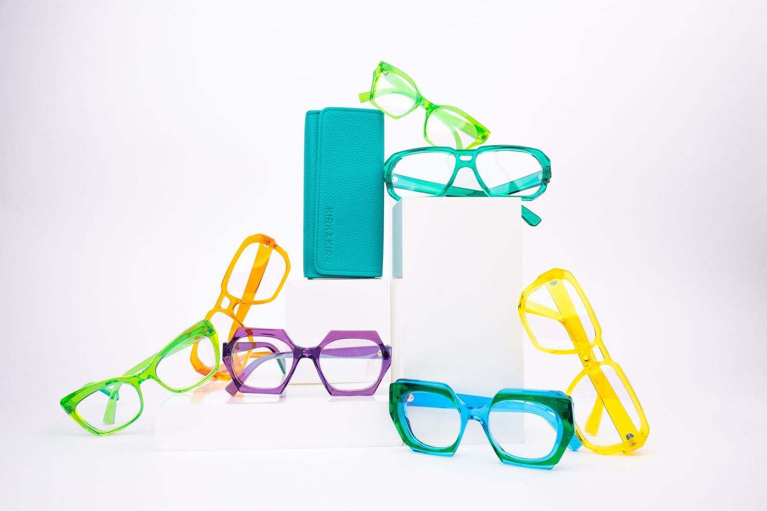 Colorful plastic eyeglass frames in green, yellow, purple, and turquoise arranged on a white background.
