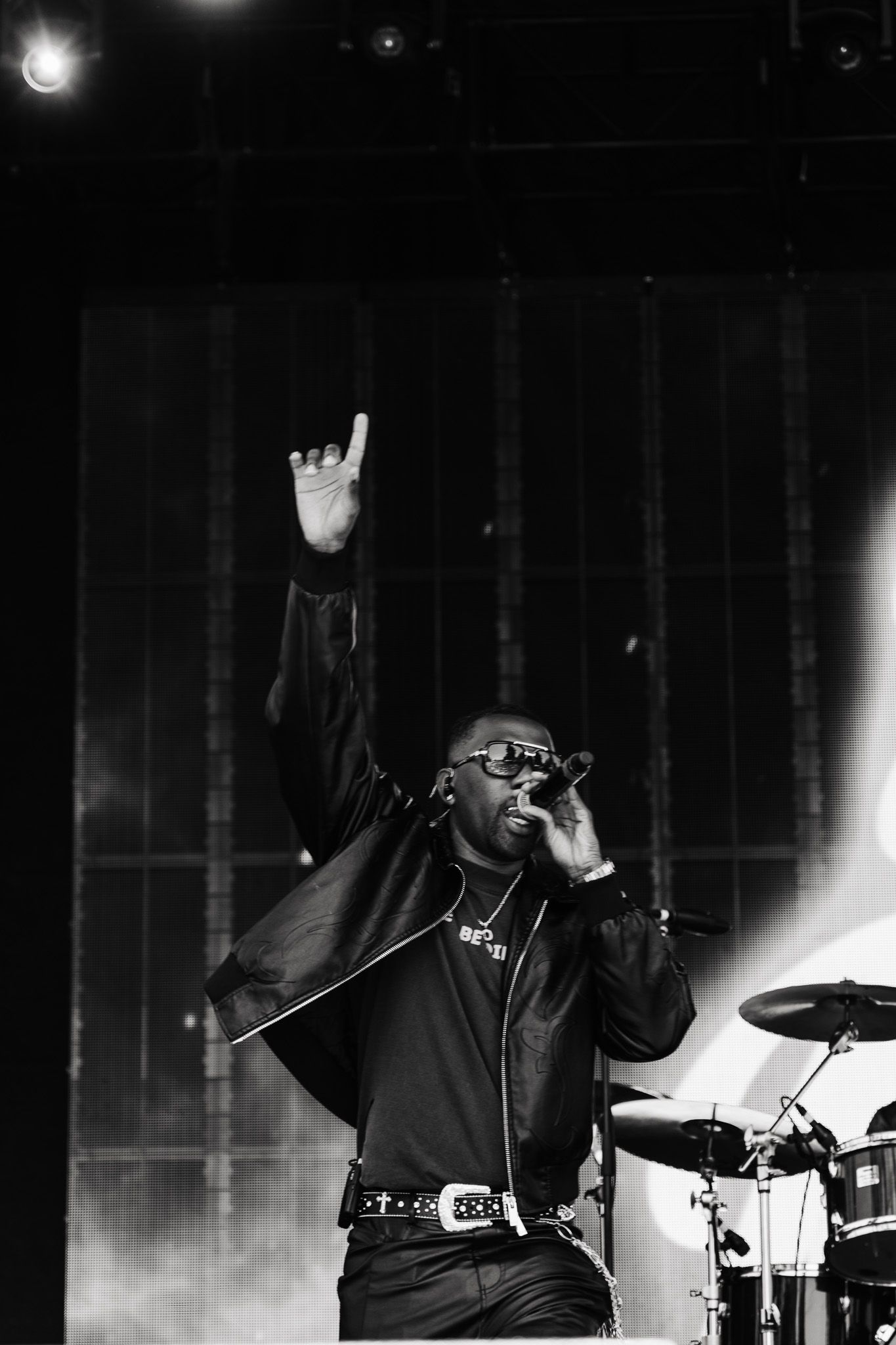 Black and white photo of a male performer singing into a mic with one hand raised at a live concert.