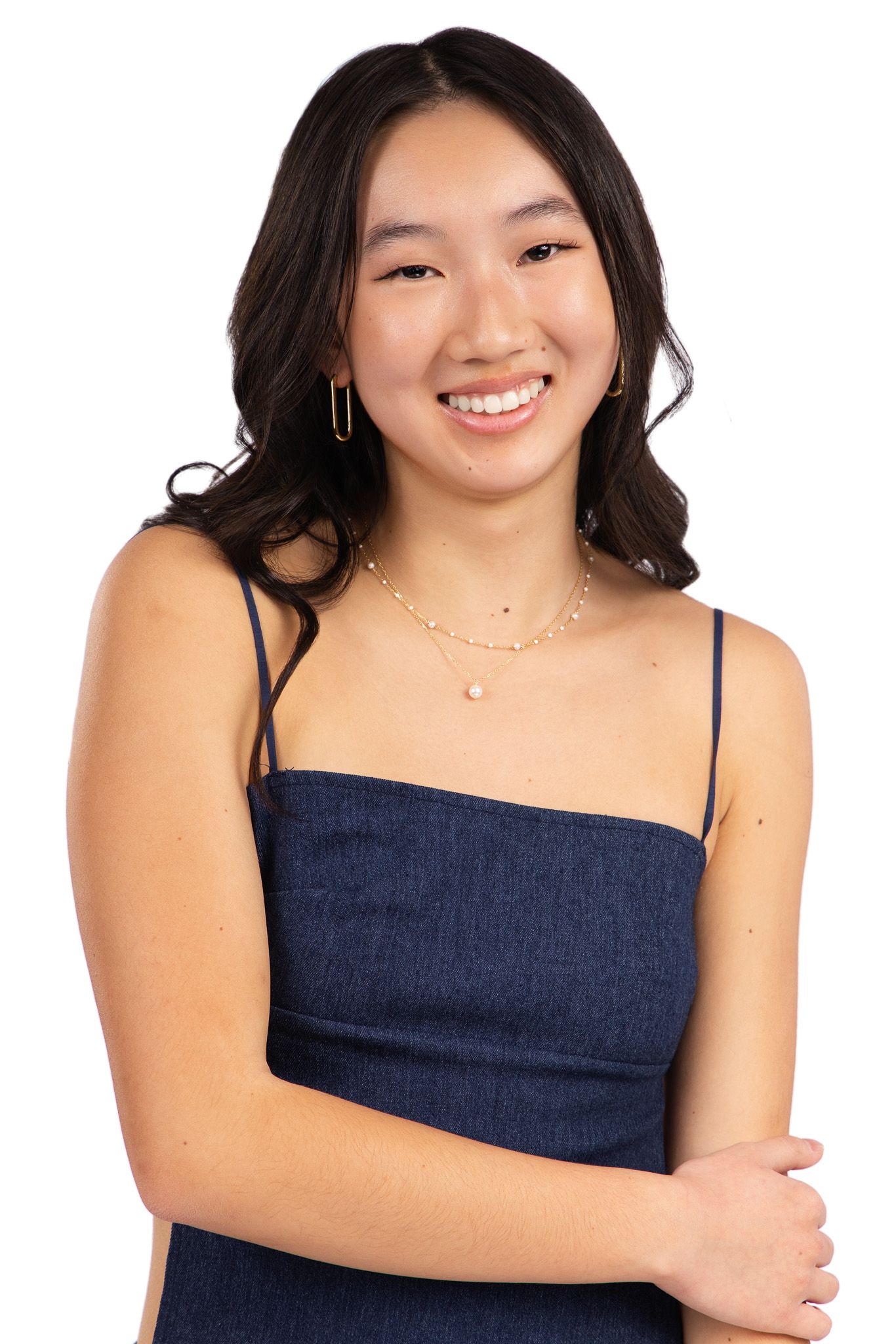 Portrait of someone in a navy blue spaghetti strap dress wearing delicate layered necklaces against white background.