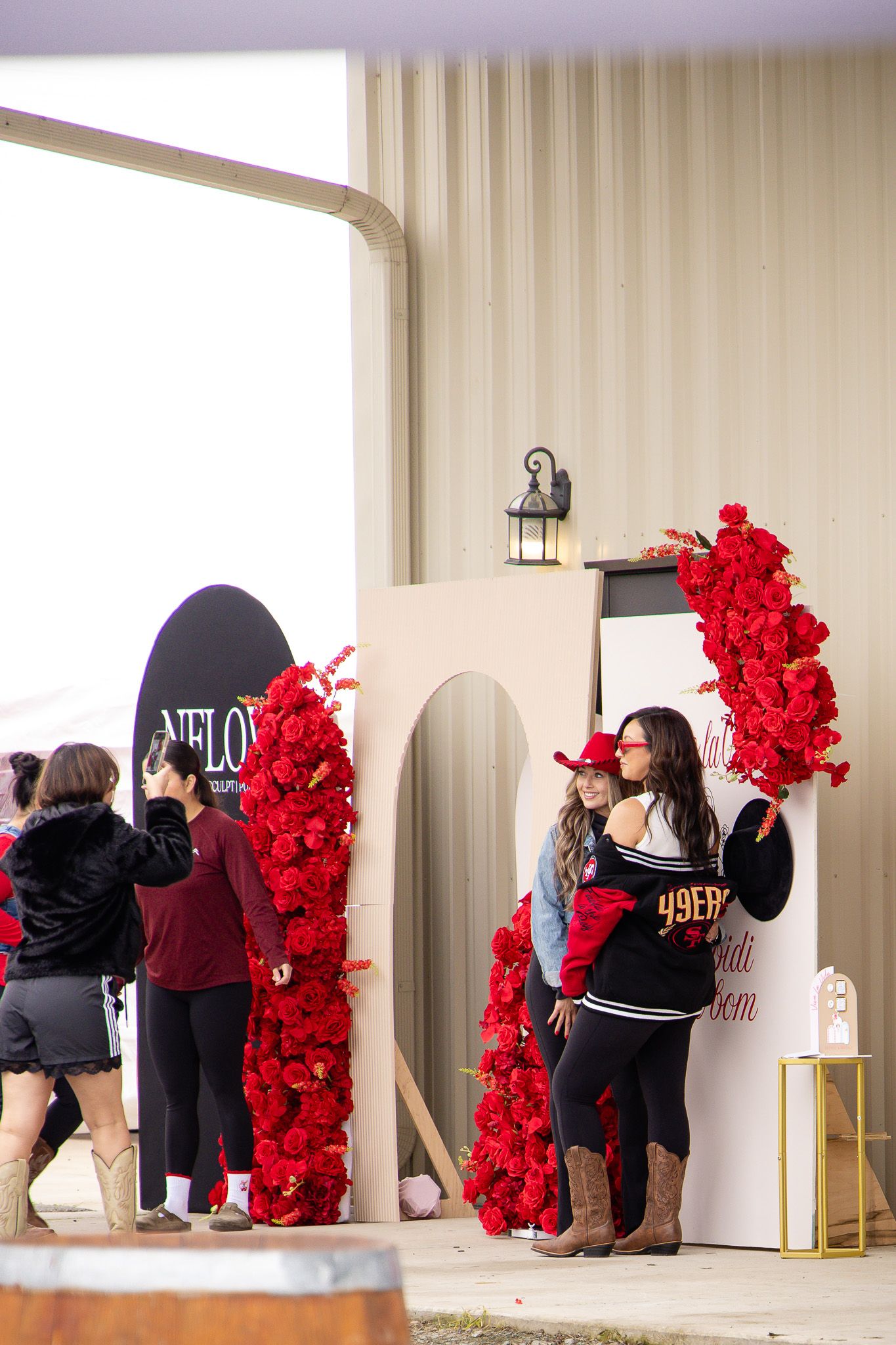 A group poses in front of a decorative red rose wall installation at an event.