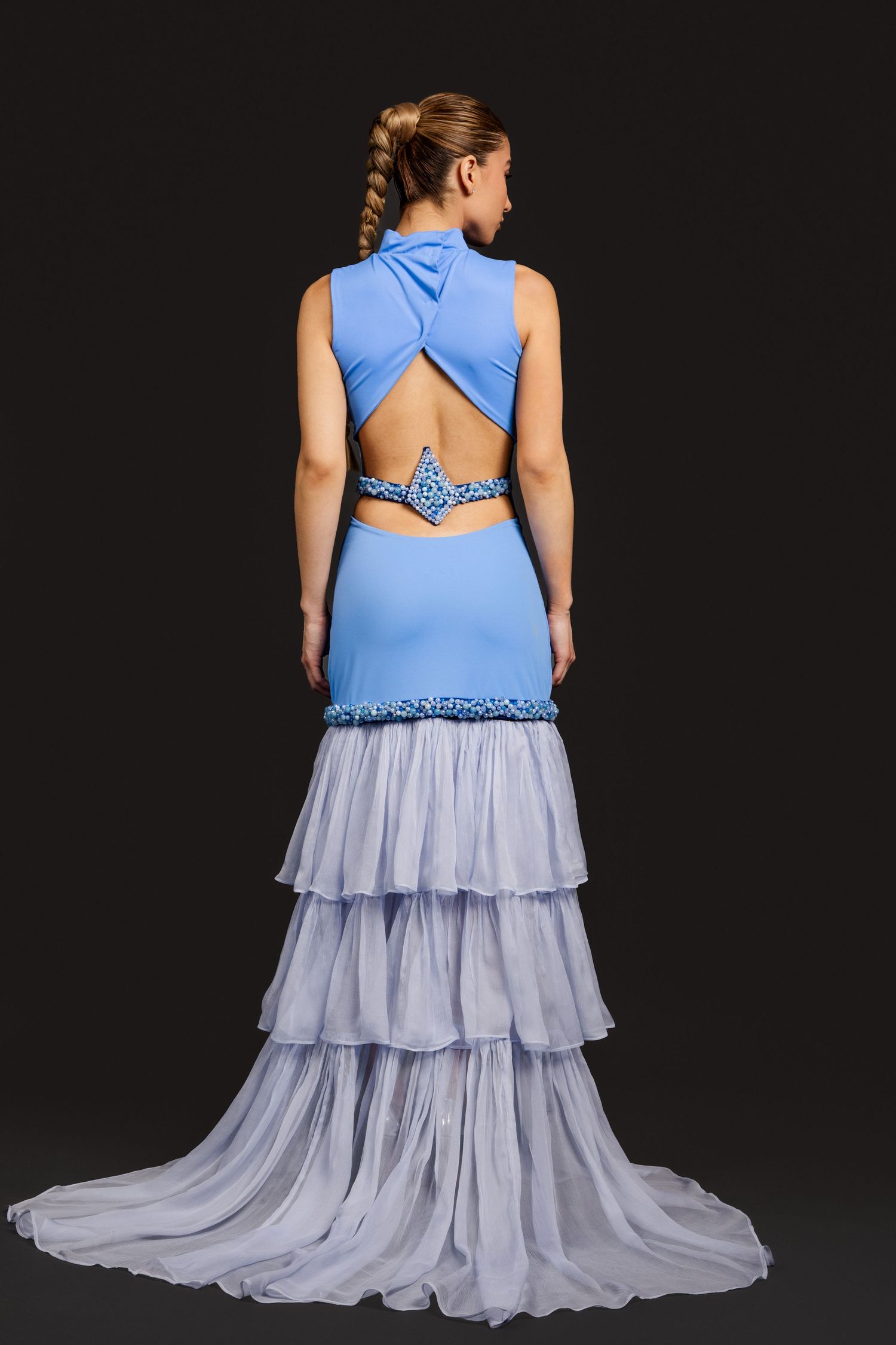 Woman in blue sleeveless gown with open back cutout and layered chiffon skirt, photographed from behind.