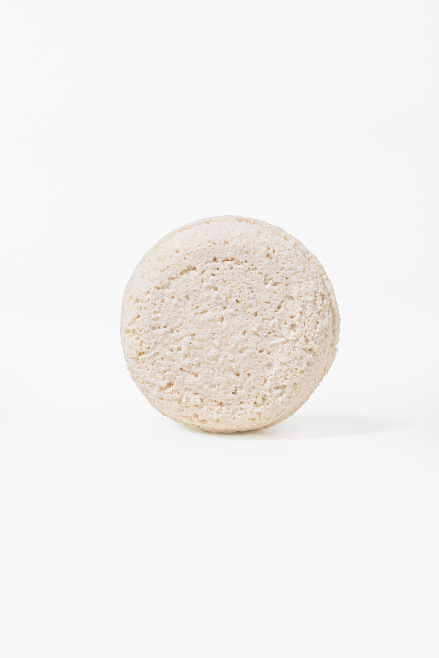 Round white shampoo bar with porous texture on white background.
