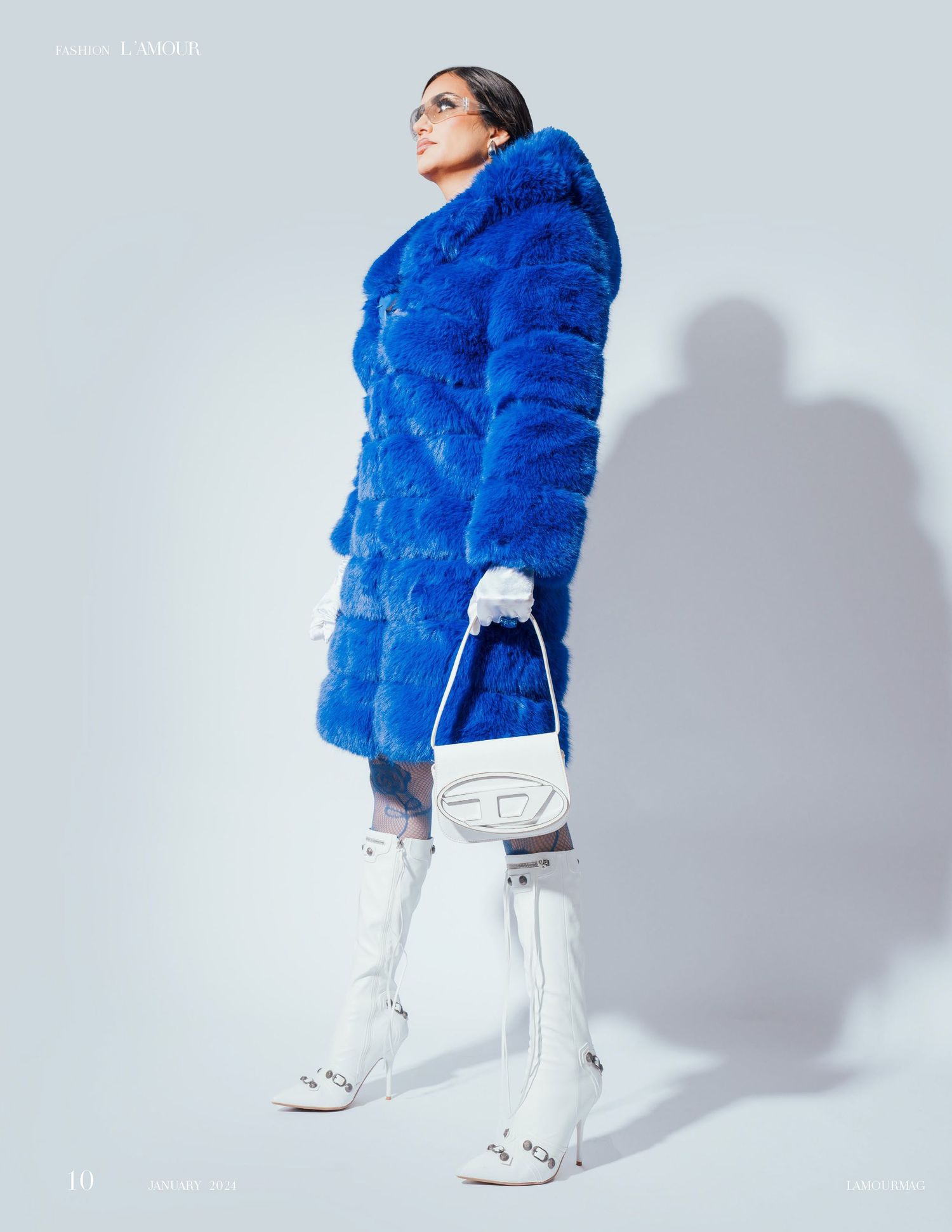 Model wearing electric blue fur coat and white pants poses against light grey backdrop.