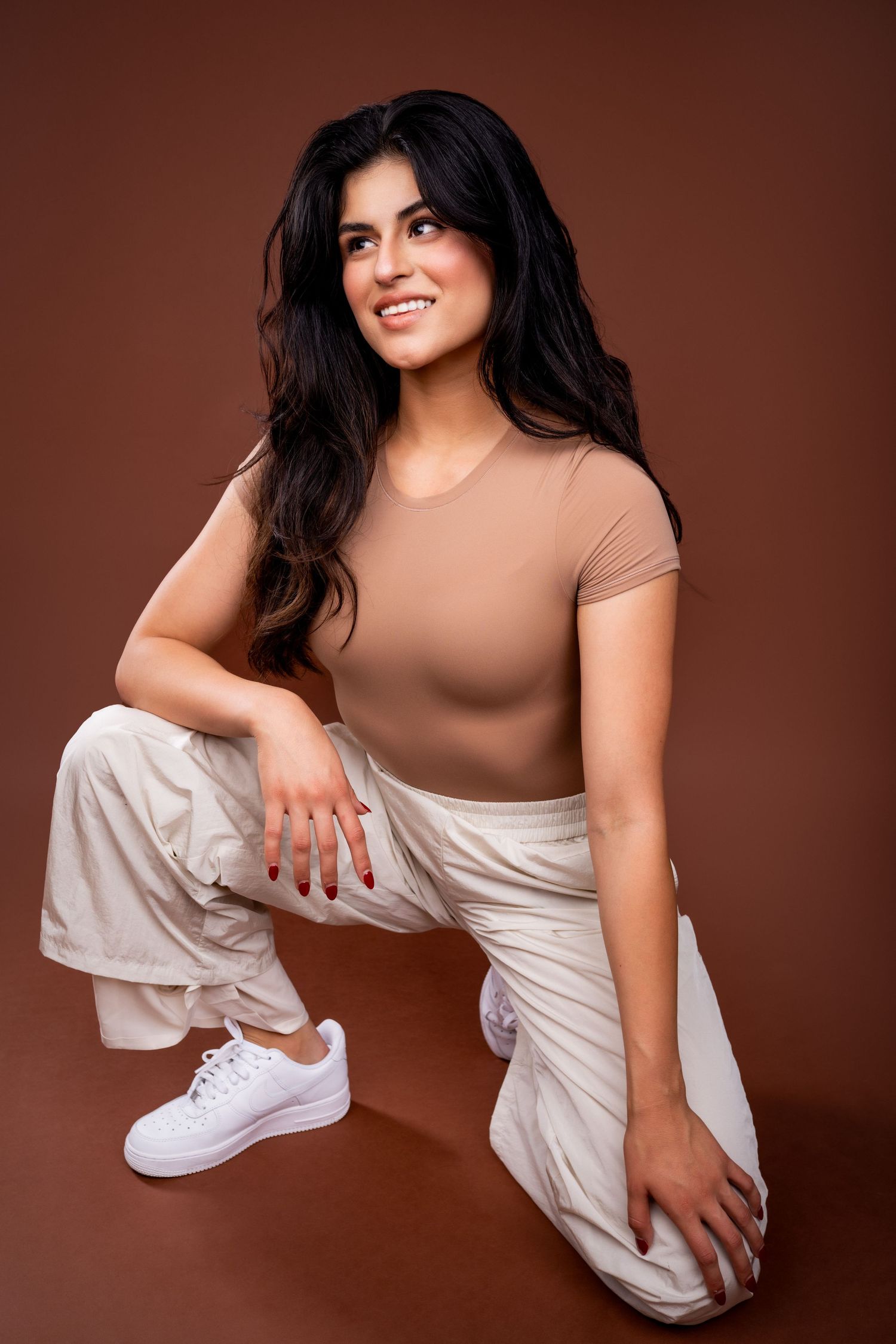 Portrait series of a person in white clothing and sneakers striking various kneeling poses against a brown background.