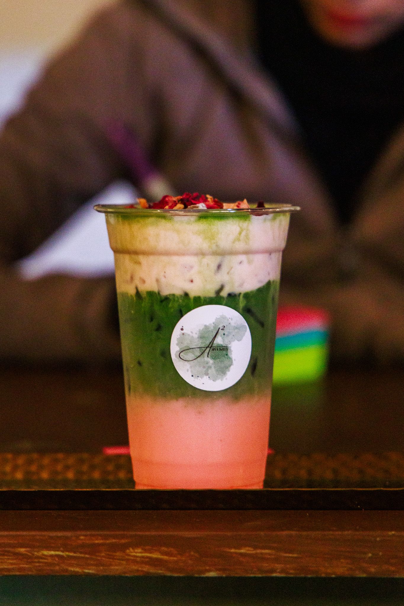 Layered matcha and strawberry iced drink in a clear cup with toppings, branded with a logo sticker.