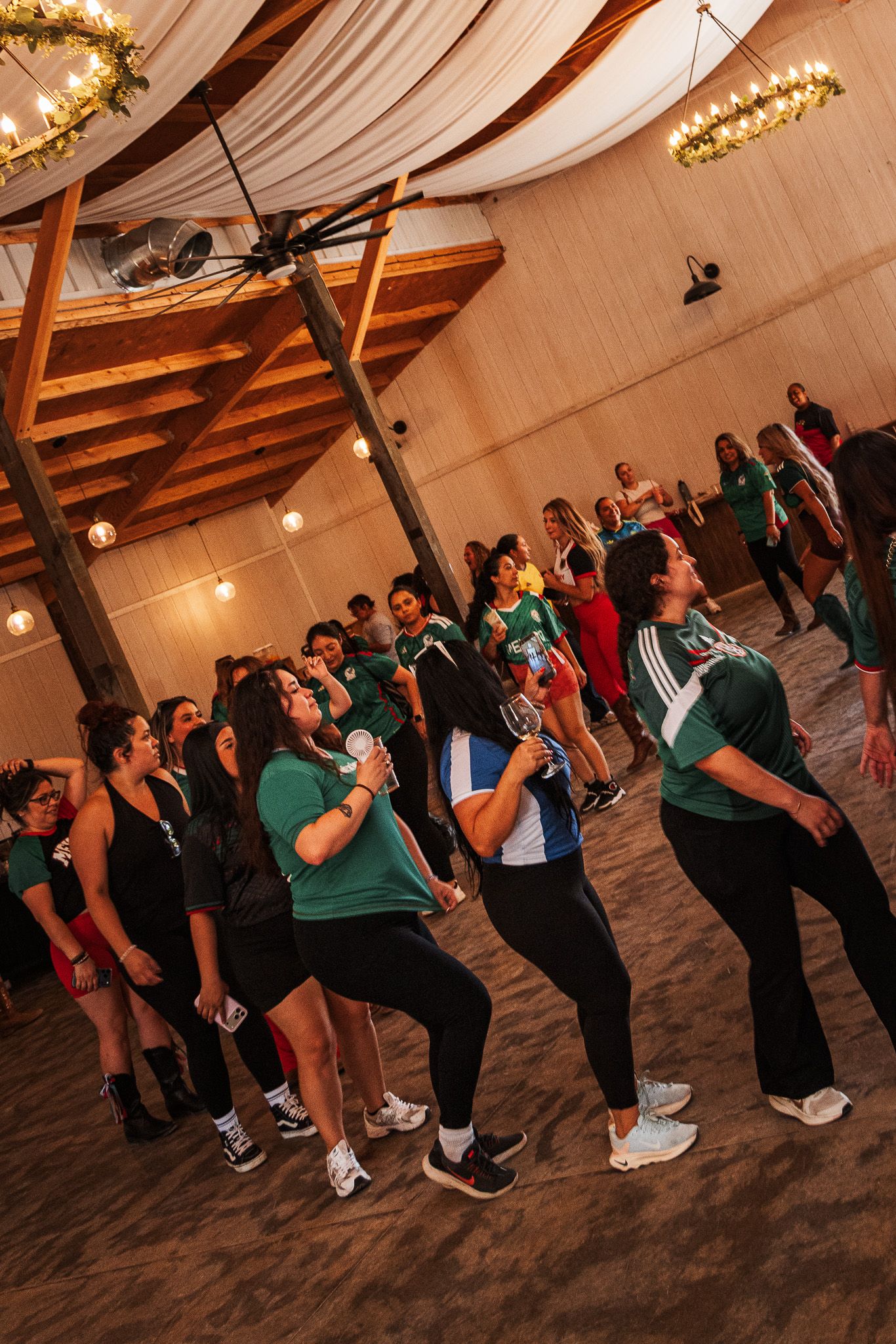 Women in green jerseys dancing energetically inside a warmly lit wooden venue during a lively group event.