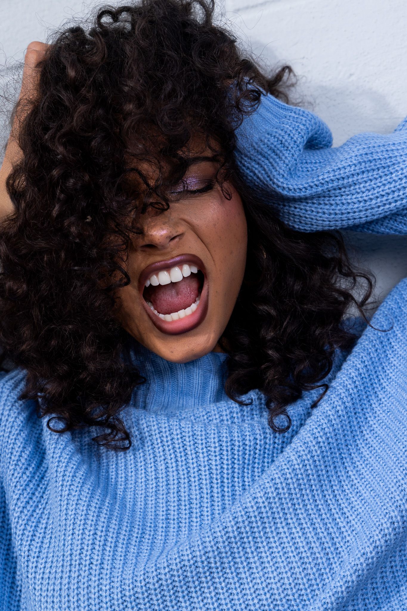 Person in blue knit sweater laughs joyfully while posing against white background.