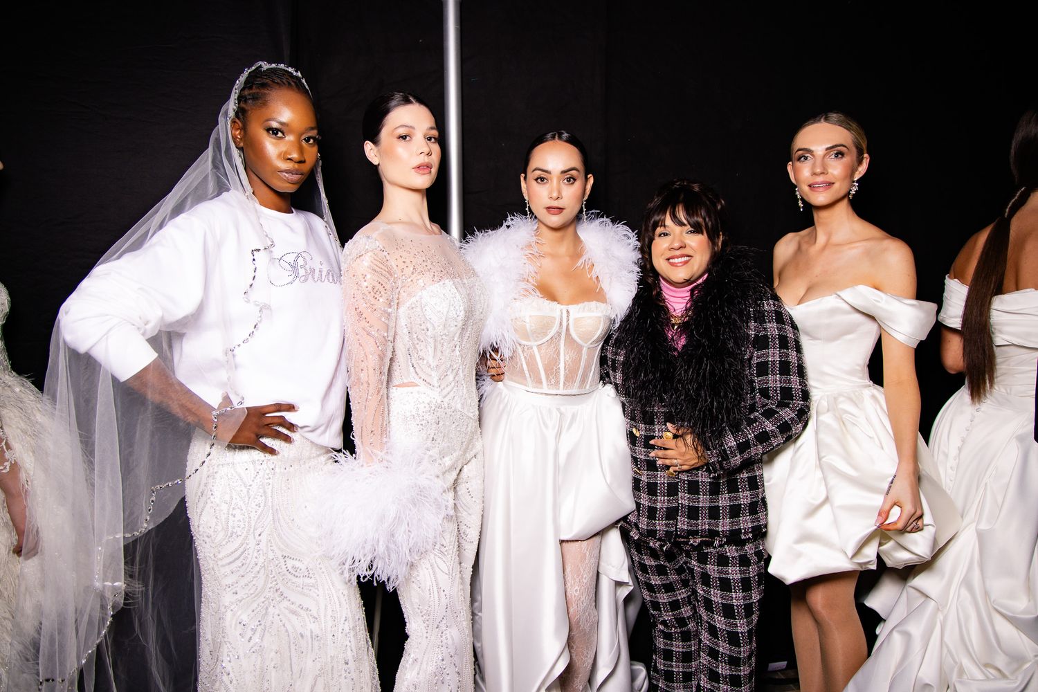 Fashion models backstage in white garments preparing for runway show.