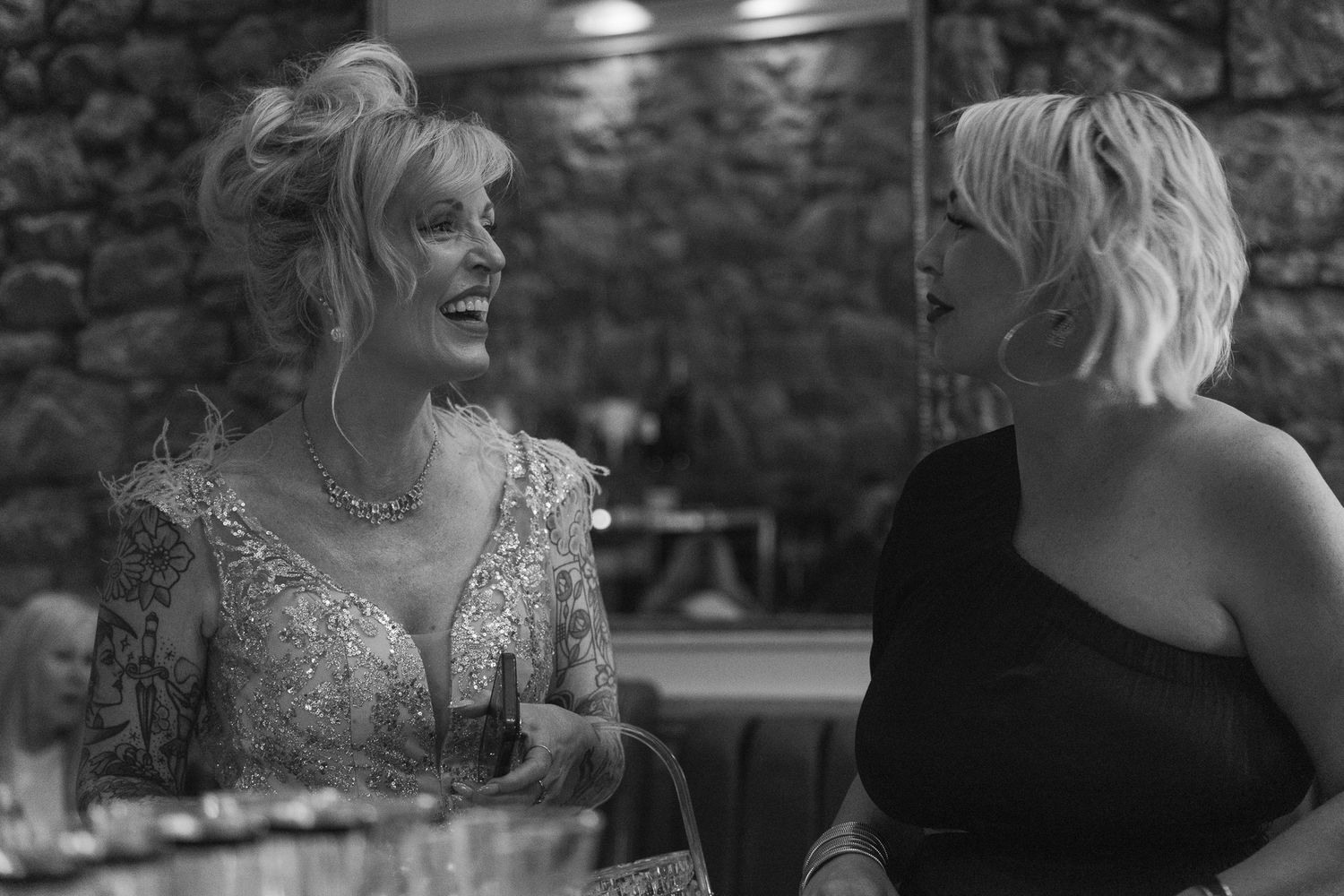 Two women laughing and conversing at an elegant event in black and white photo.