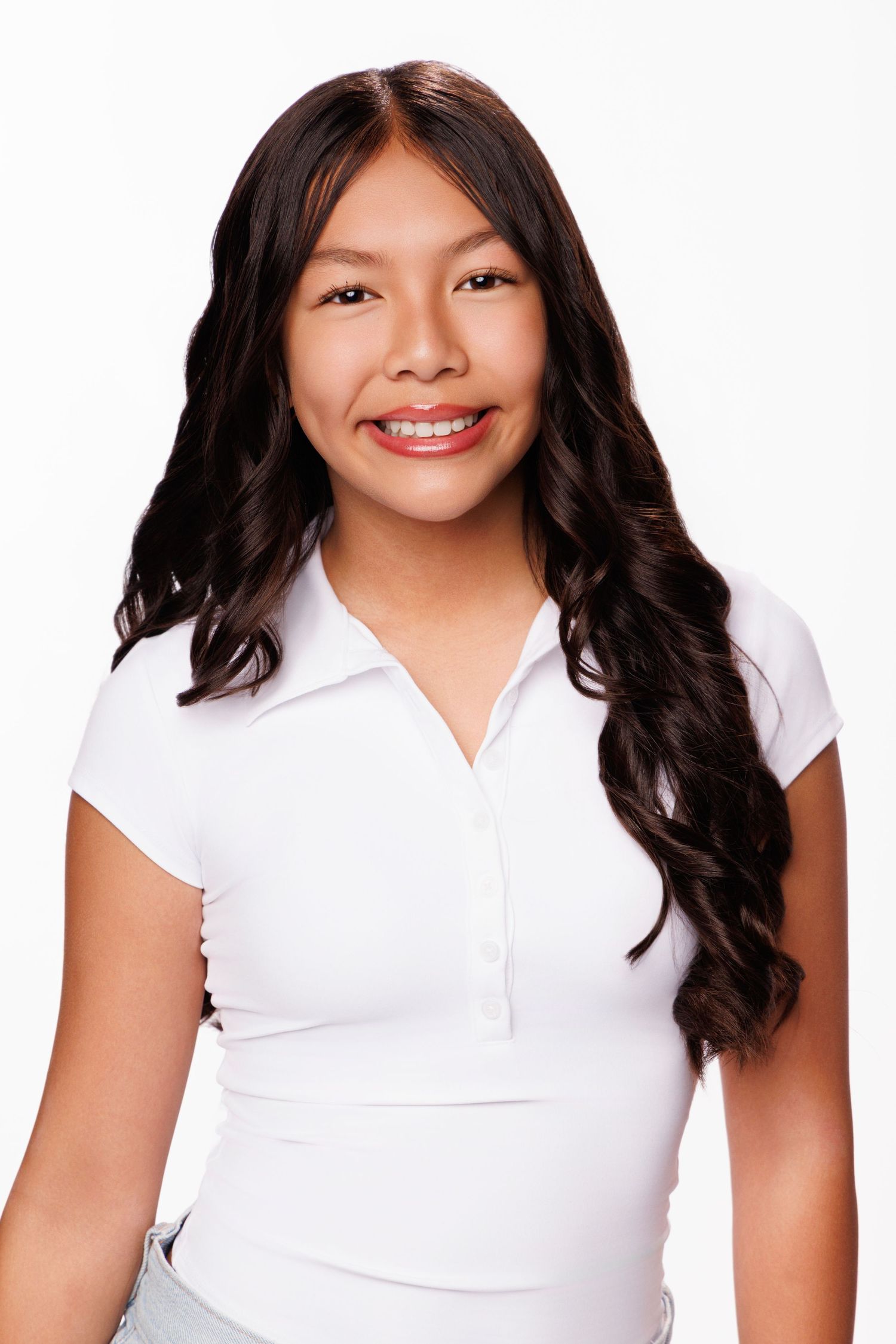 Young woman with long wavy dark hair smiling, wearing a white polo shirt against a white background.