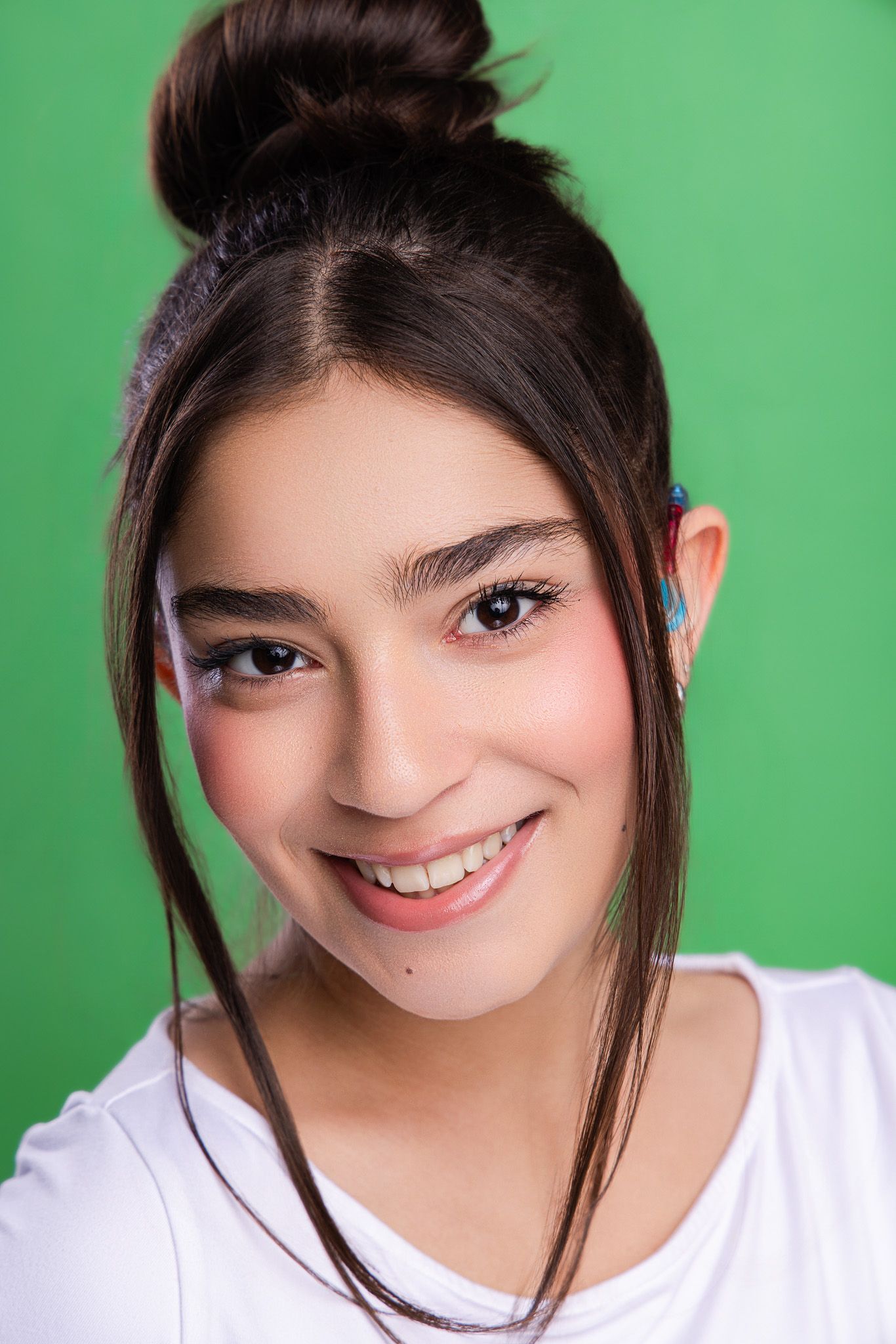 Happy teenage girl with dark hair in a bun smiling, wearing a white top against a green background.