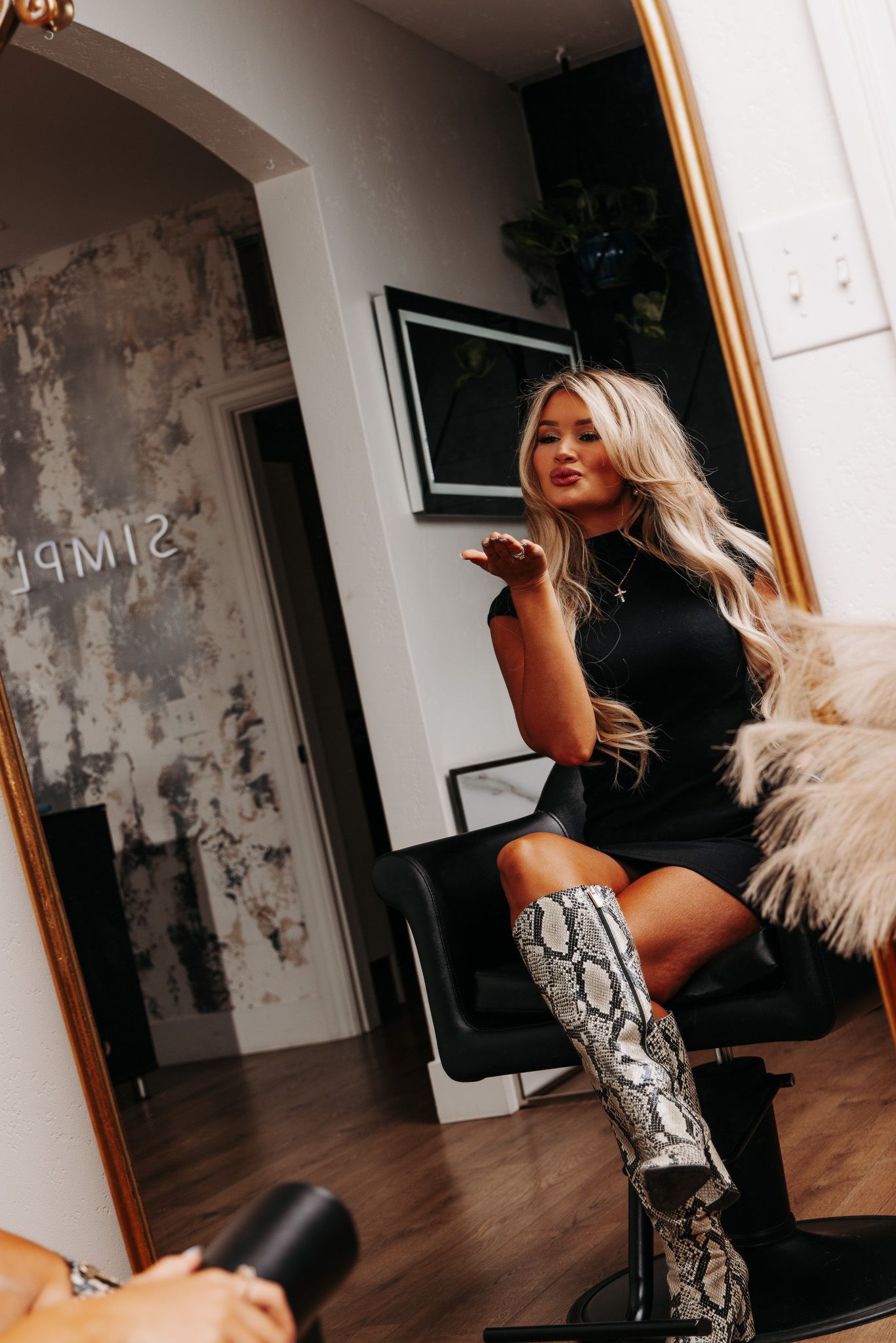 Model in black outfit and snakeskin boots poses dramatically on hardwood floor.
