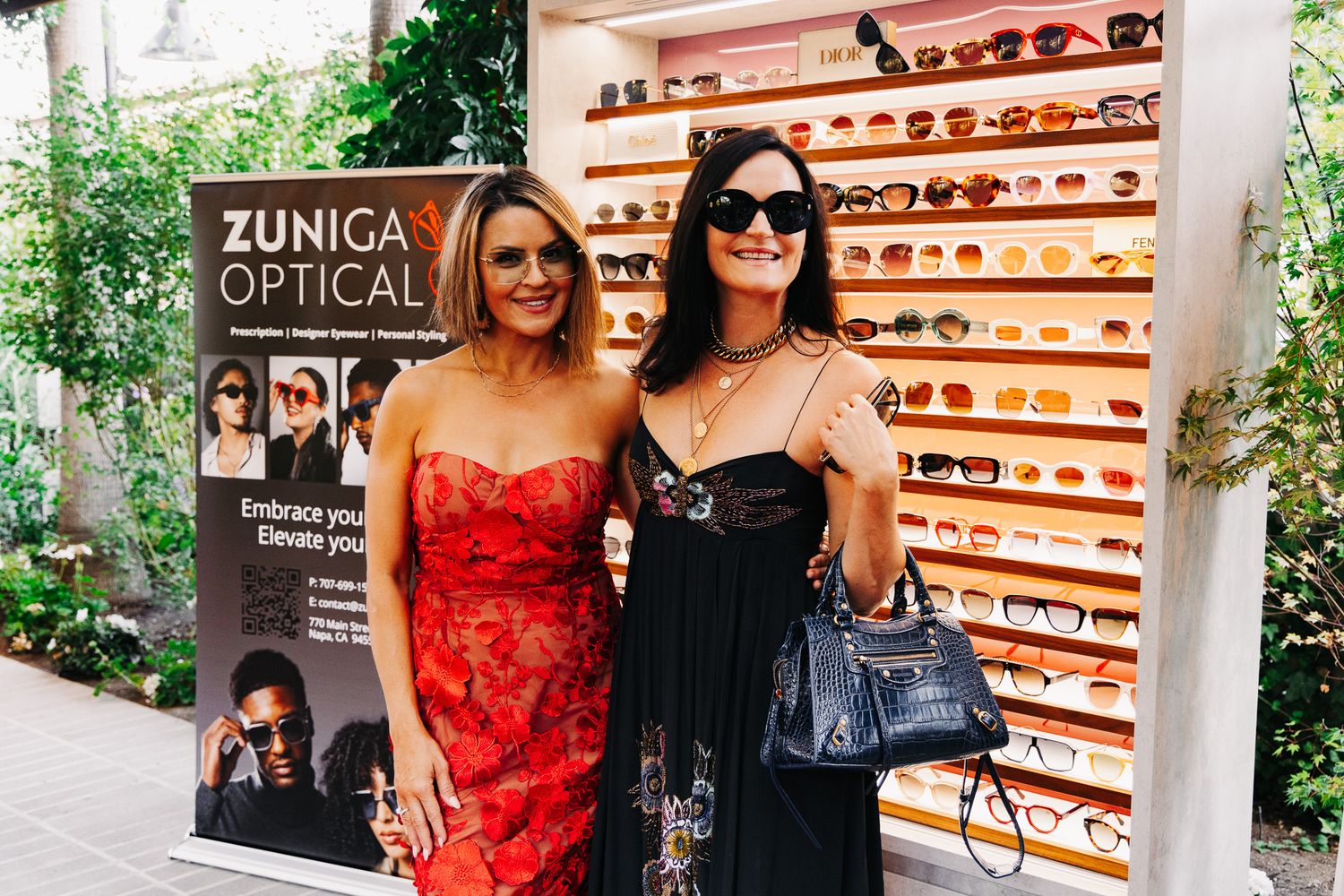Two people browse eyewear displays at an optical store with wooden shelving and warm lighting.
