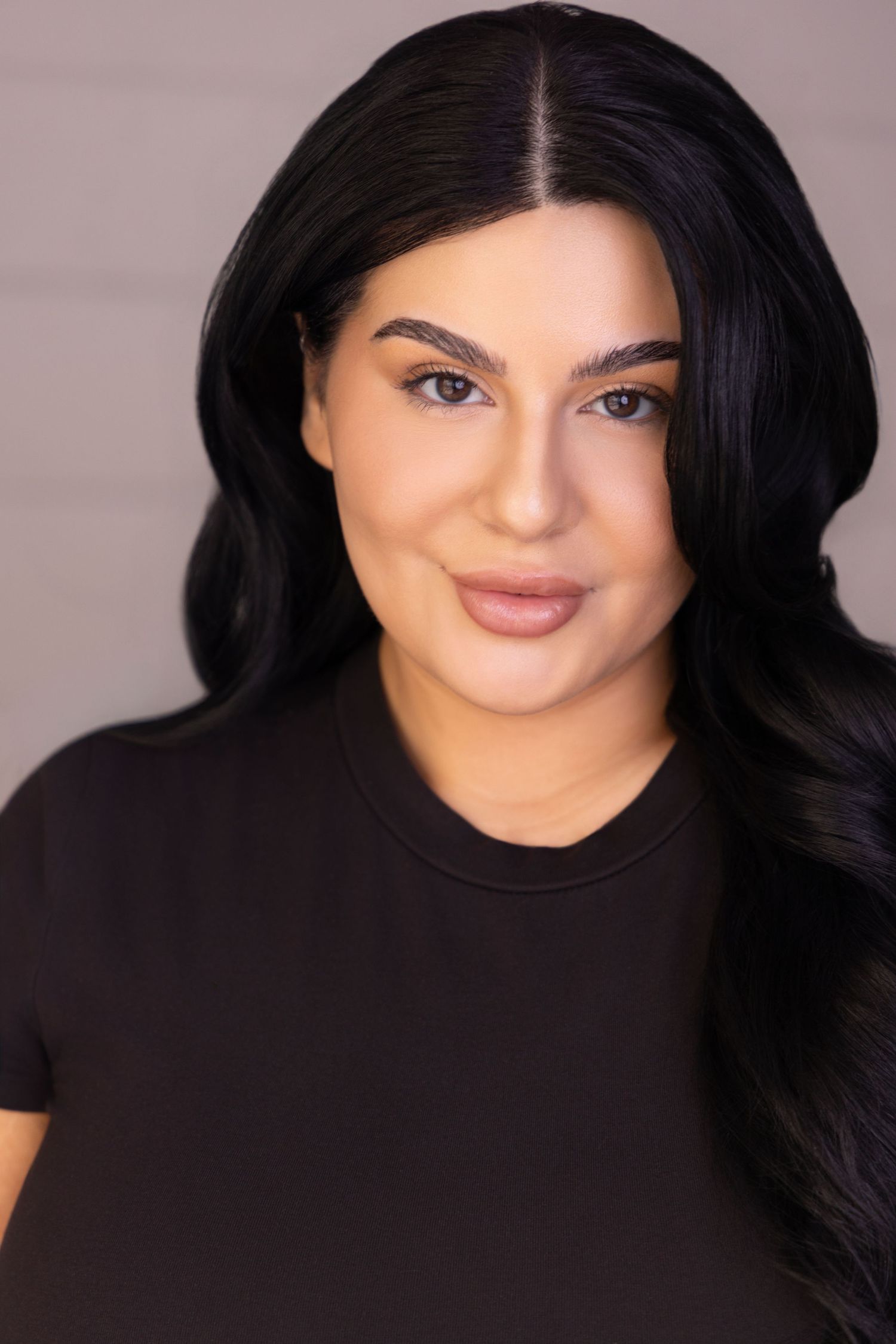 Portrait of someone with long black wavy hair wearing dark clothing against a neutral background.