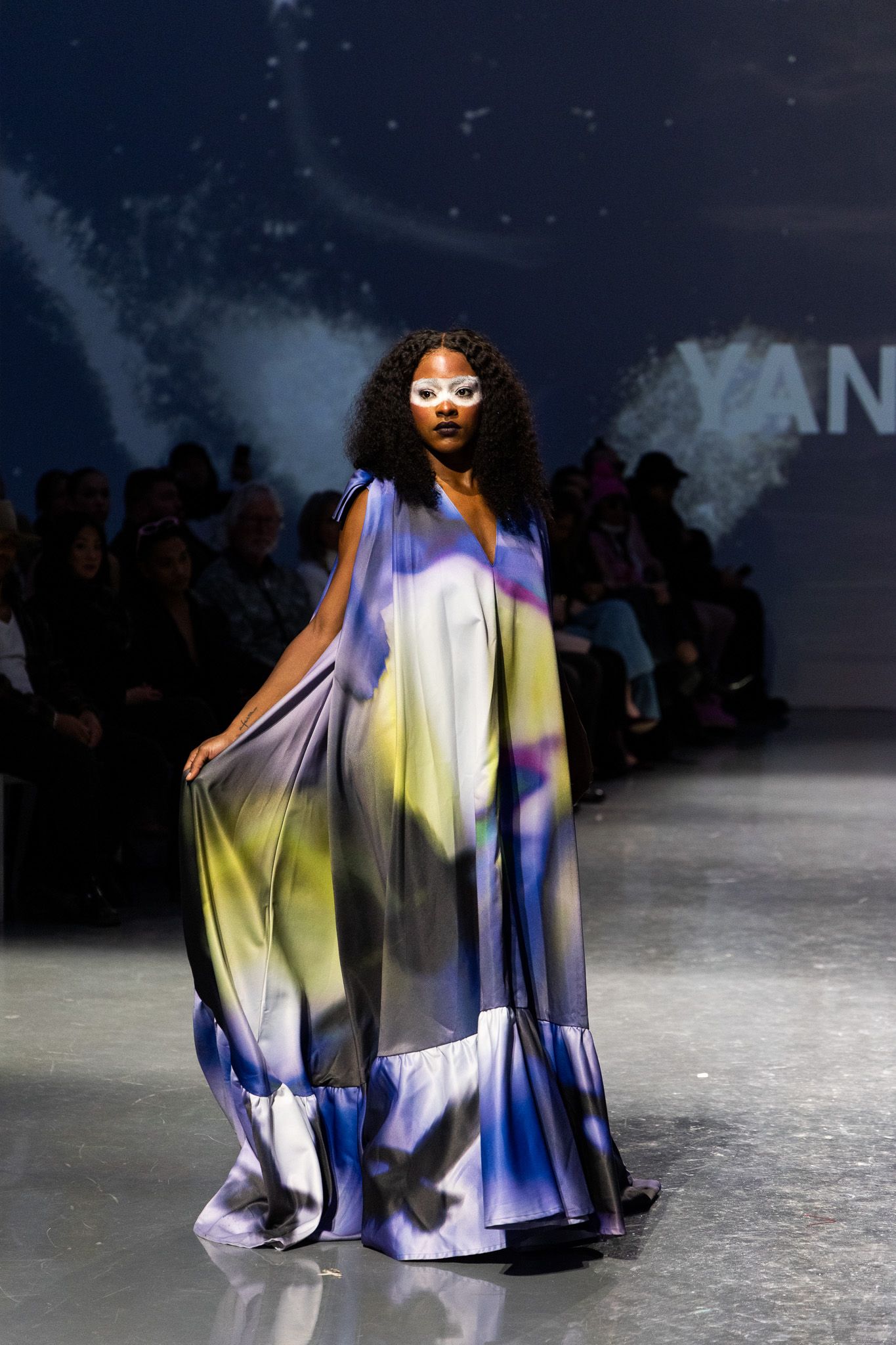 Runway show featuring flowing multicolored garments with dramatic lighting effects.