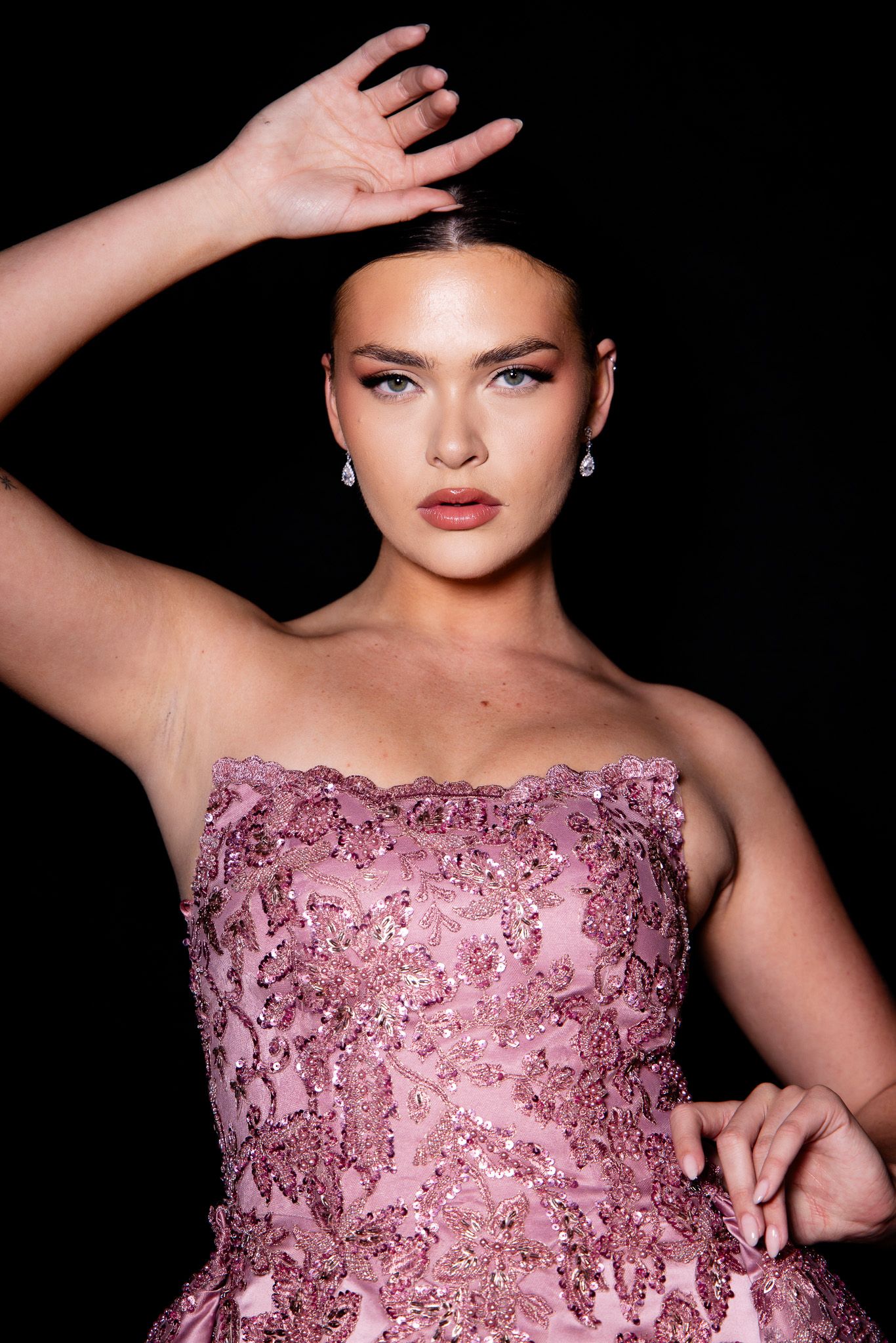 Model showcases a stunning pink beaded evening gown with strapless neckline against dark backdrop.