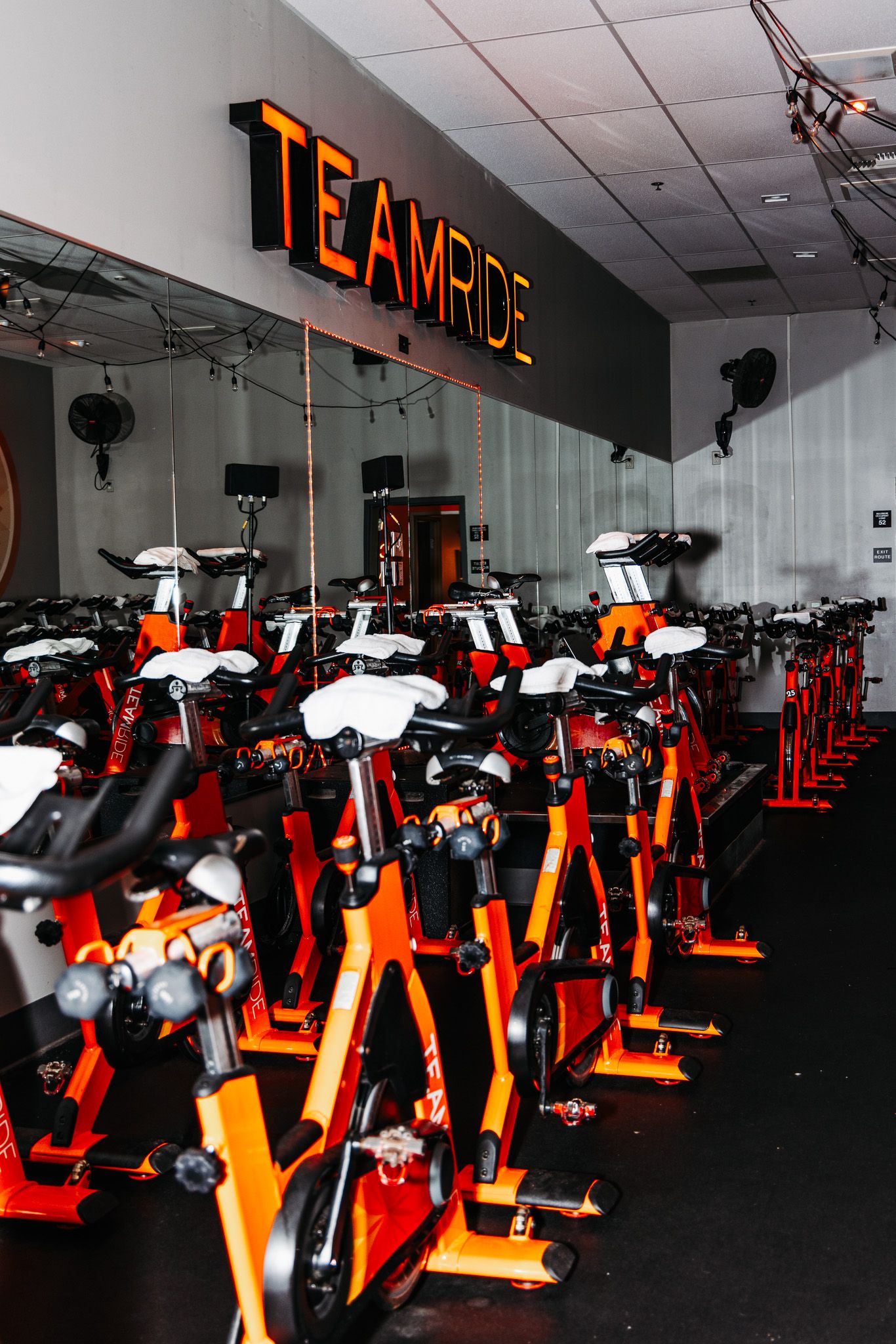 Row of orange and black stationary exercise bikes in a modern cycling studio with illuminated TeamEdge sign.
