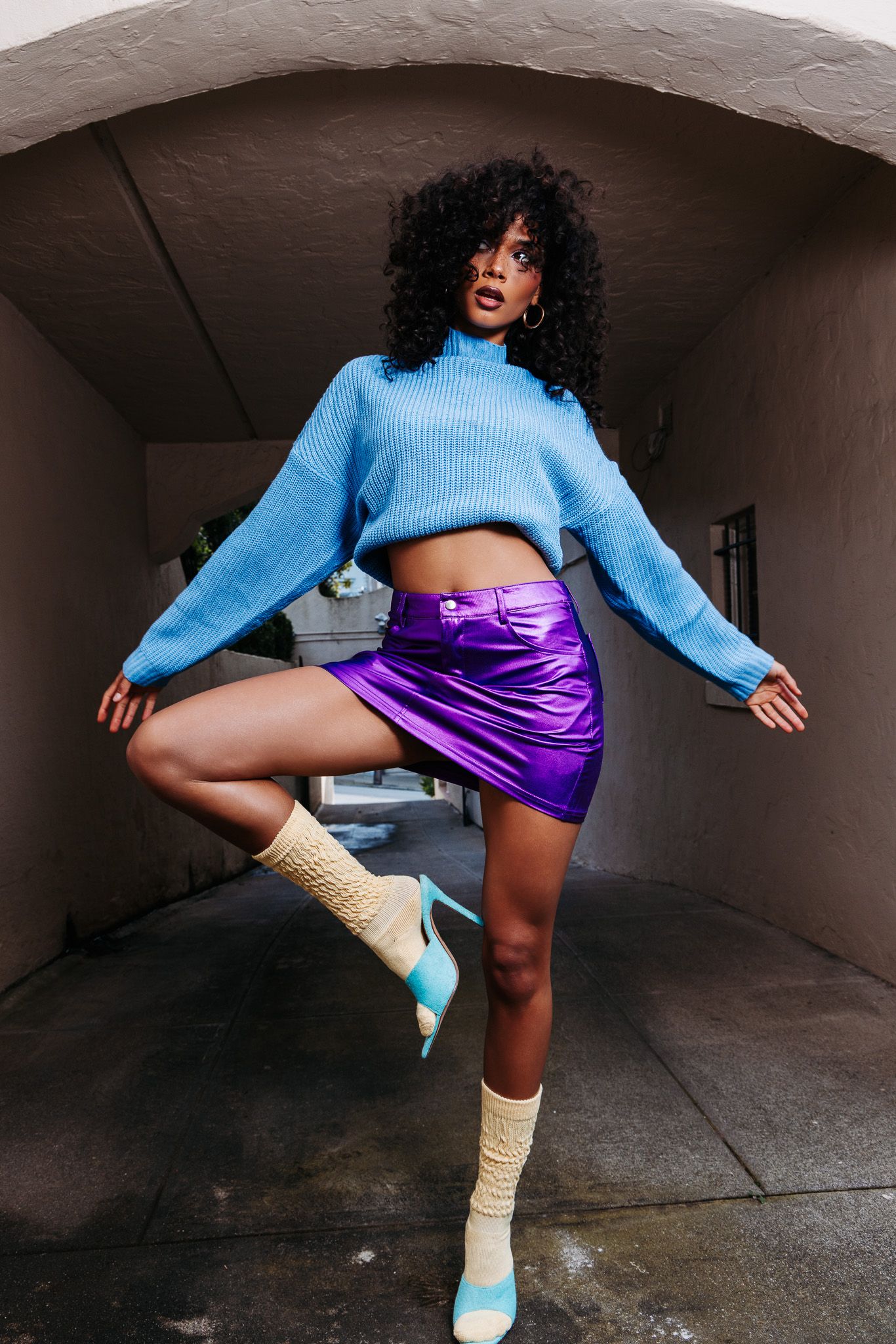 Stylish outfit featuring a blue cropped sweater, purple metallic skirt and cream socks with turquoise heels.