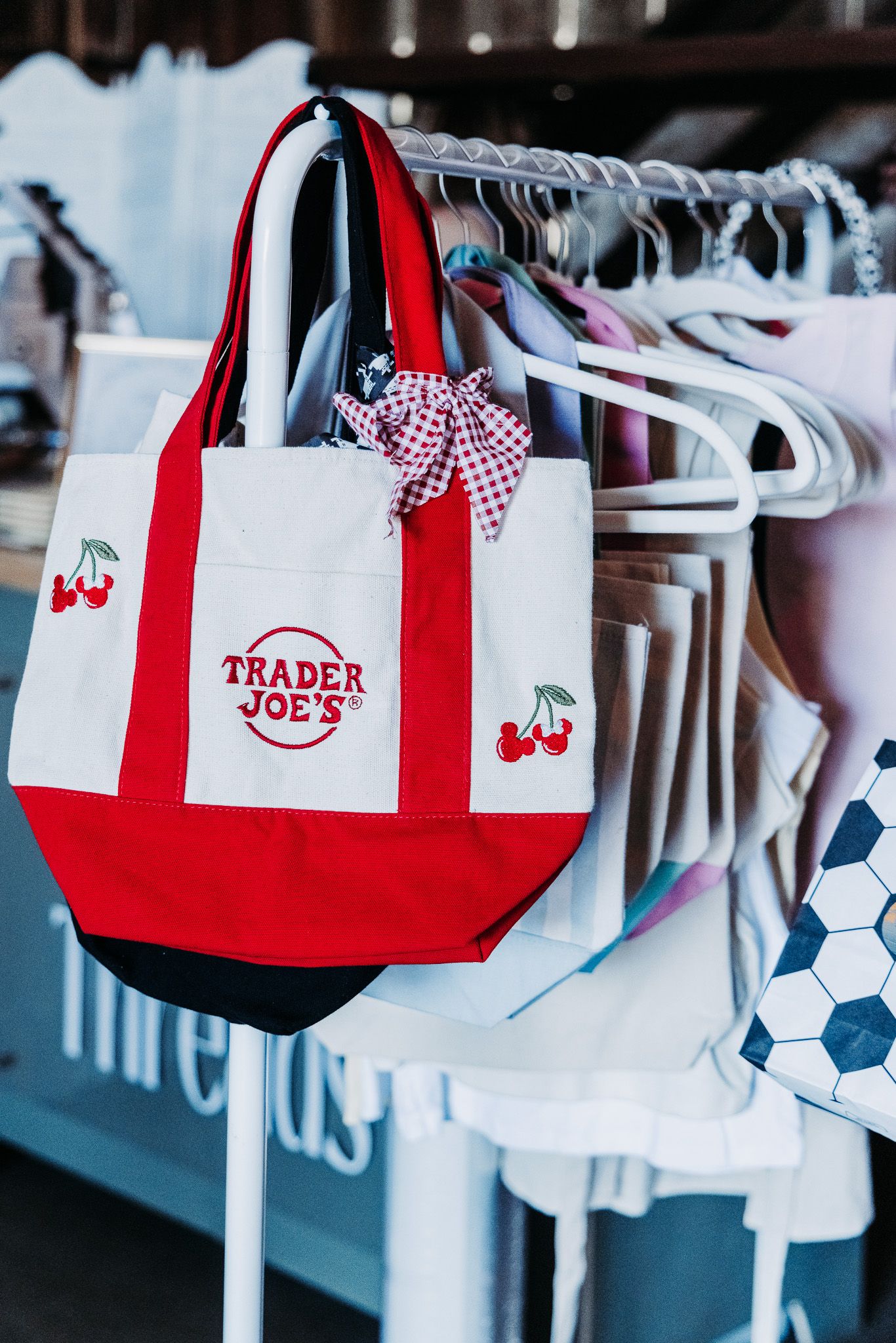 Trader Joe's red and white canvas tote bag with cherry embroidery hanging on a clothing rack.