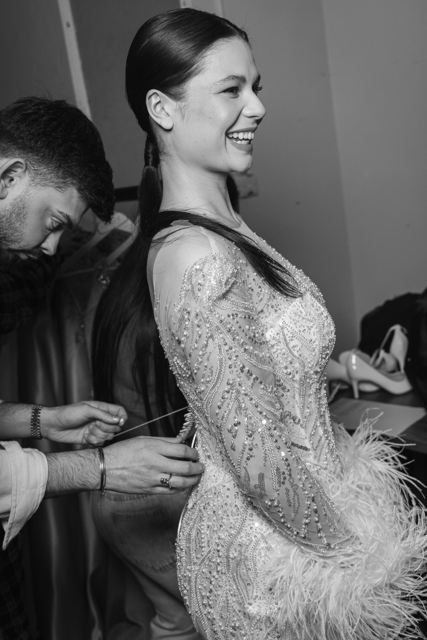 Black and white photos capturing backstage moments of a model getting ready in an embellished feathered gown.