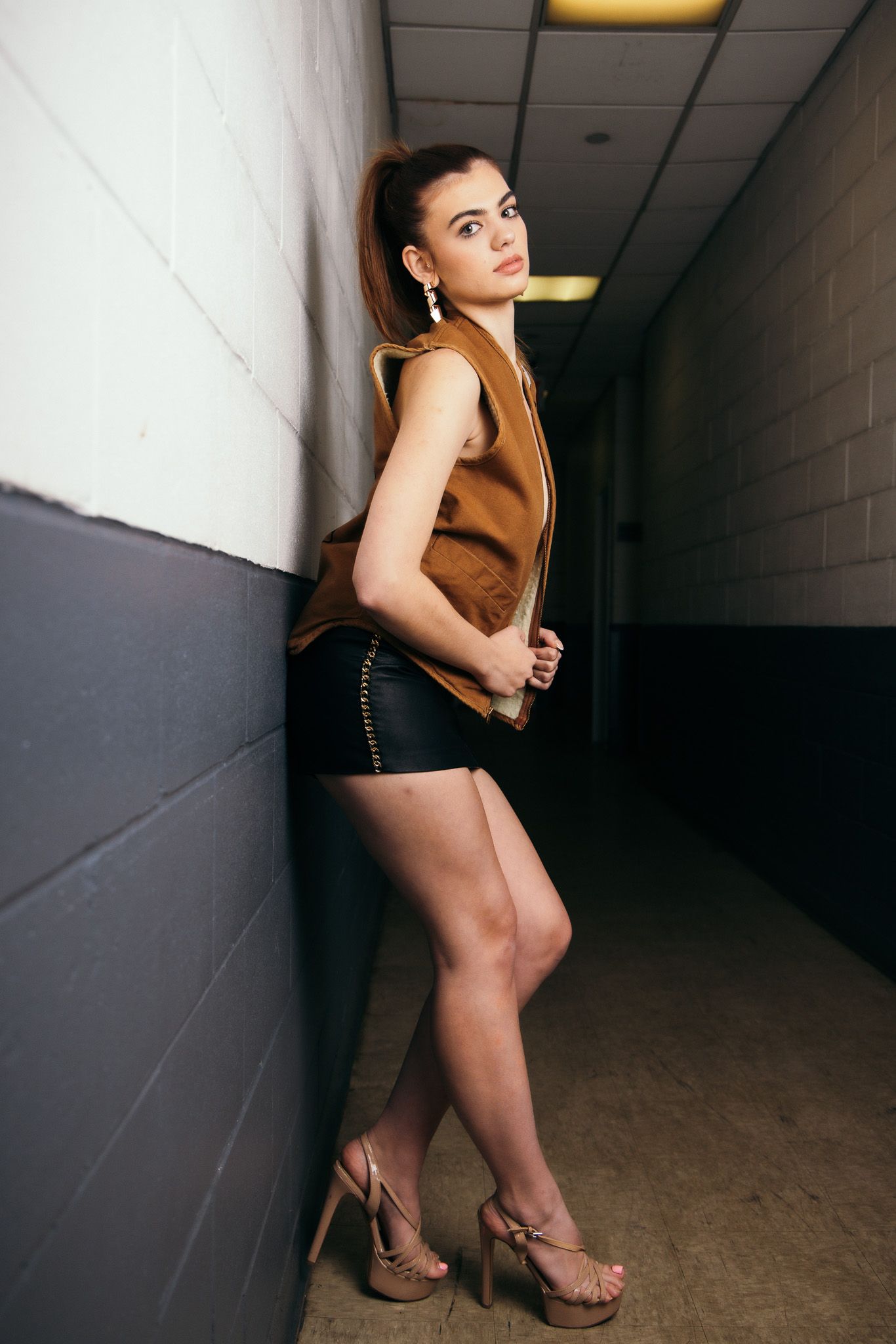 Model in brown top poses dramatically in dimly lit hallway setting.