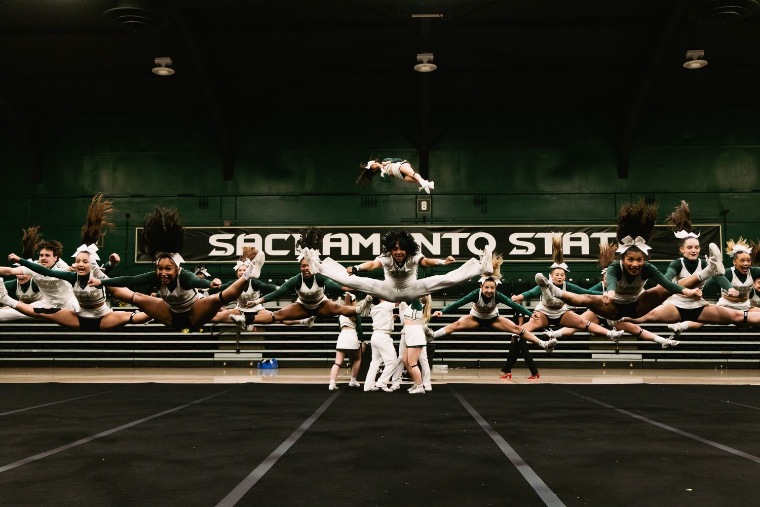 Sacramento State cheerleaders performing synchronized jumps and stunts on a gymnasium floor during a cheer routine.