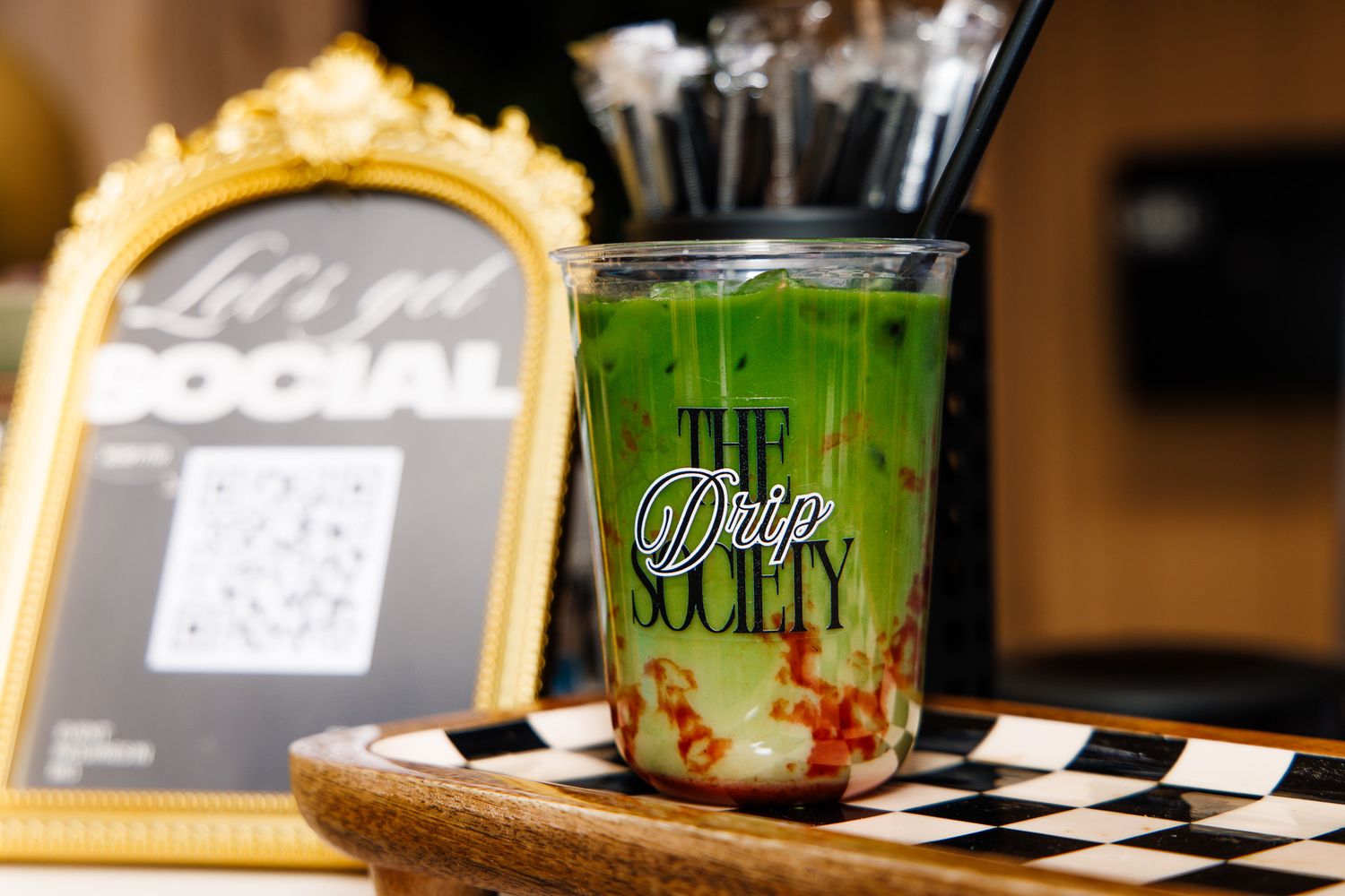 A green matcha iced drink in a branded The Drip Society cup on a checkered surface.