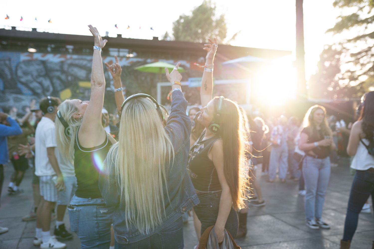 Crowd of young people dancing outdoors at a sunset festival event with golden backlight.