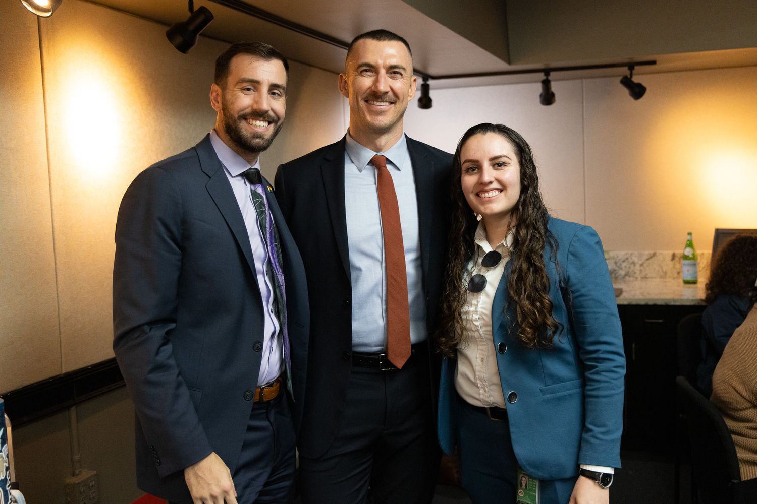 Business professionals pose together for a group photo in an office hallway with warm lighting.