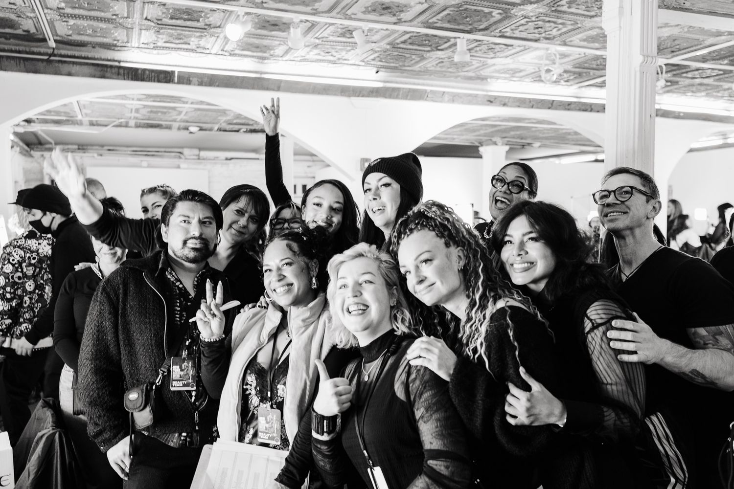 A black and white panoramic image showing a joyful crowd of people laughing and socializing at an indoor event.