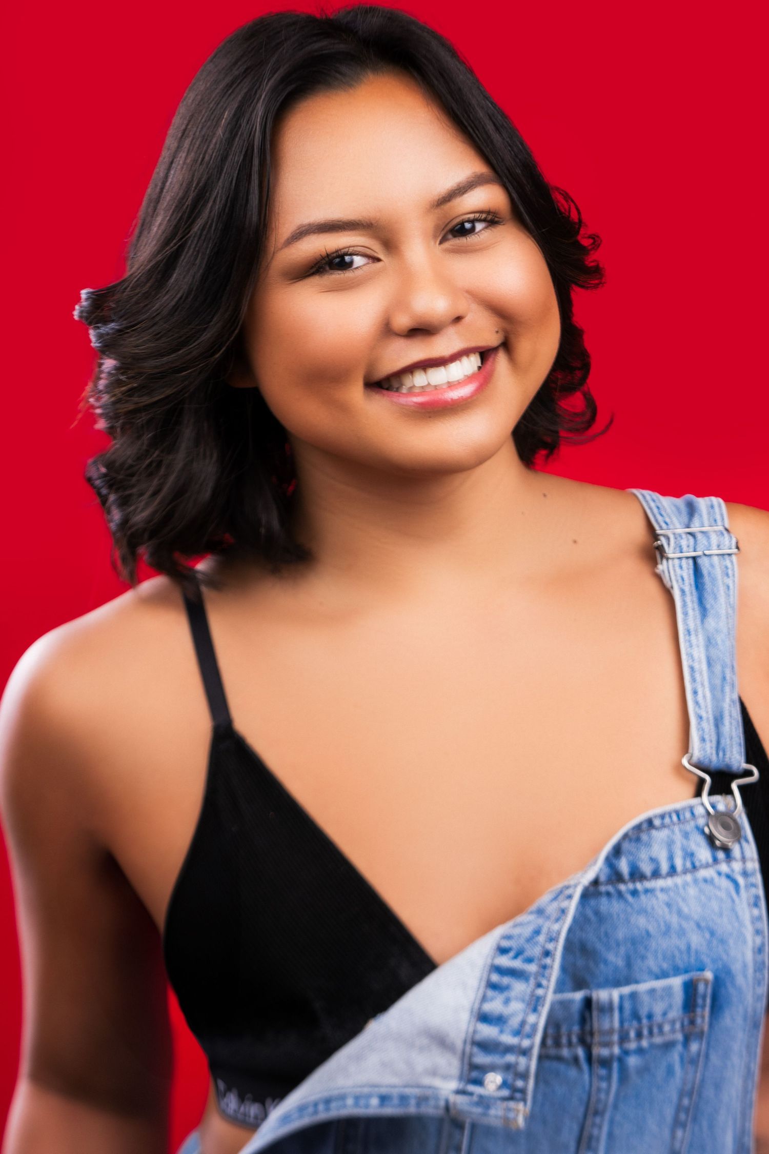 Casual portrait against a red background featuring denim overalls and a black top.