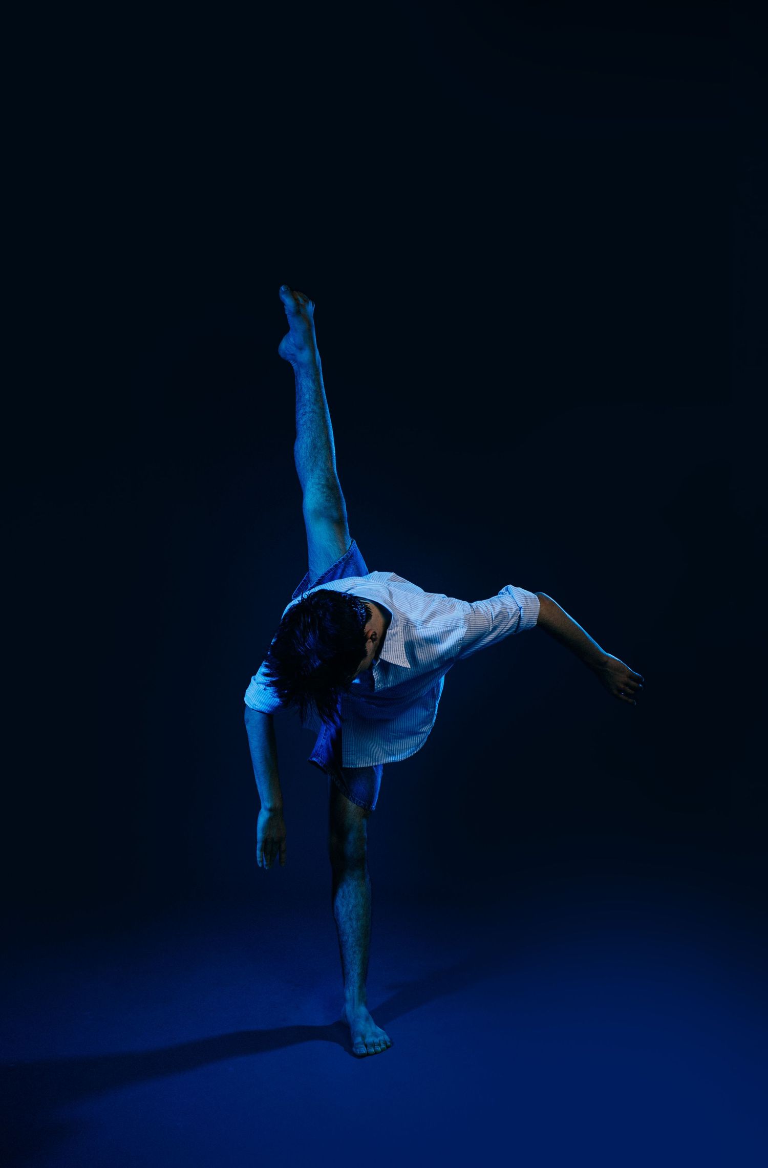 Graceful dance movements captured in dramatic blue lighting against a black background showcase artistic expression.