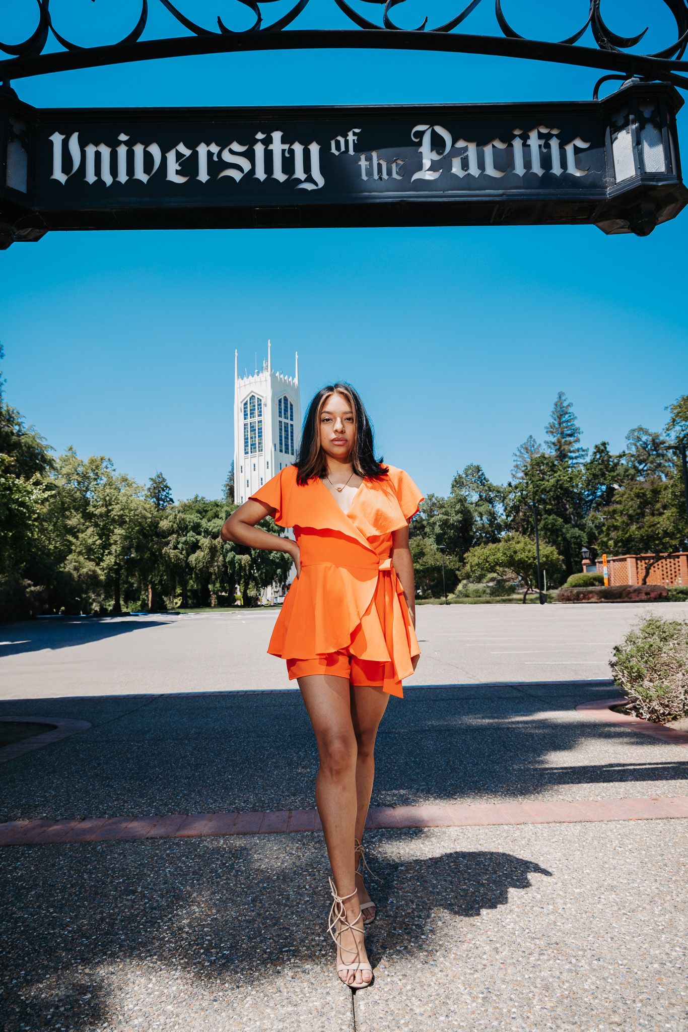 A person in a bright orange romper poses on campus at University of the Pacific with a tower visible in the background.
