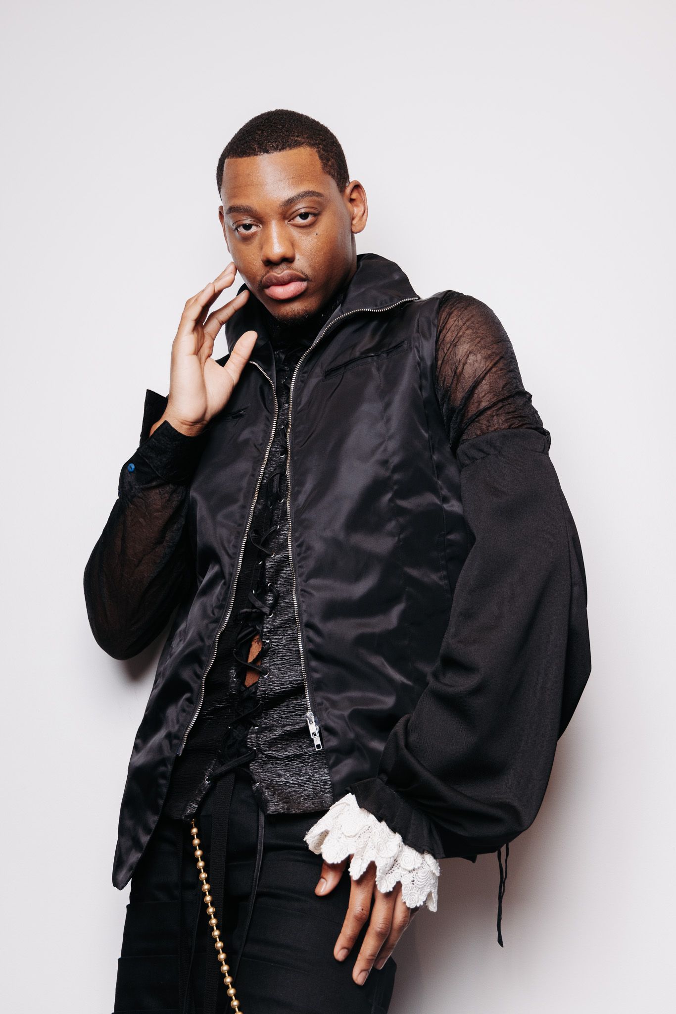 Fashion portrait of model wearing oversized black bomber jacket and white gloves against white background.