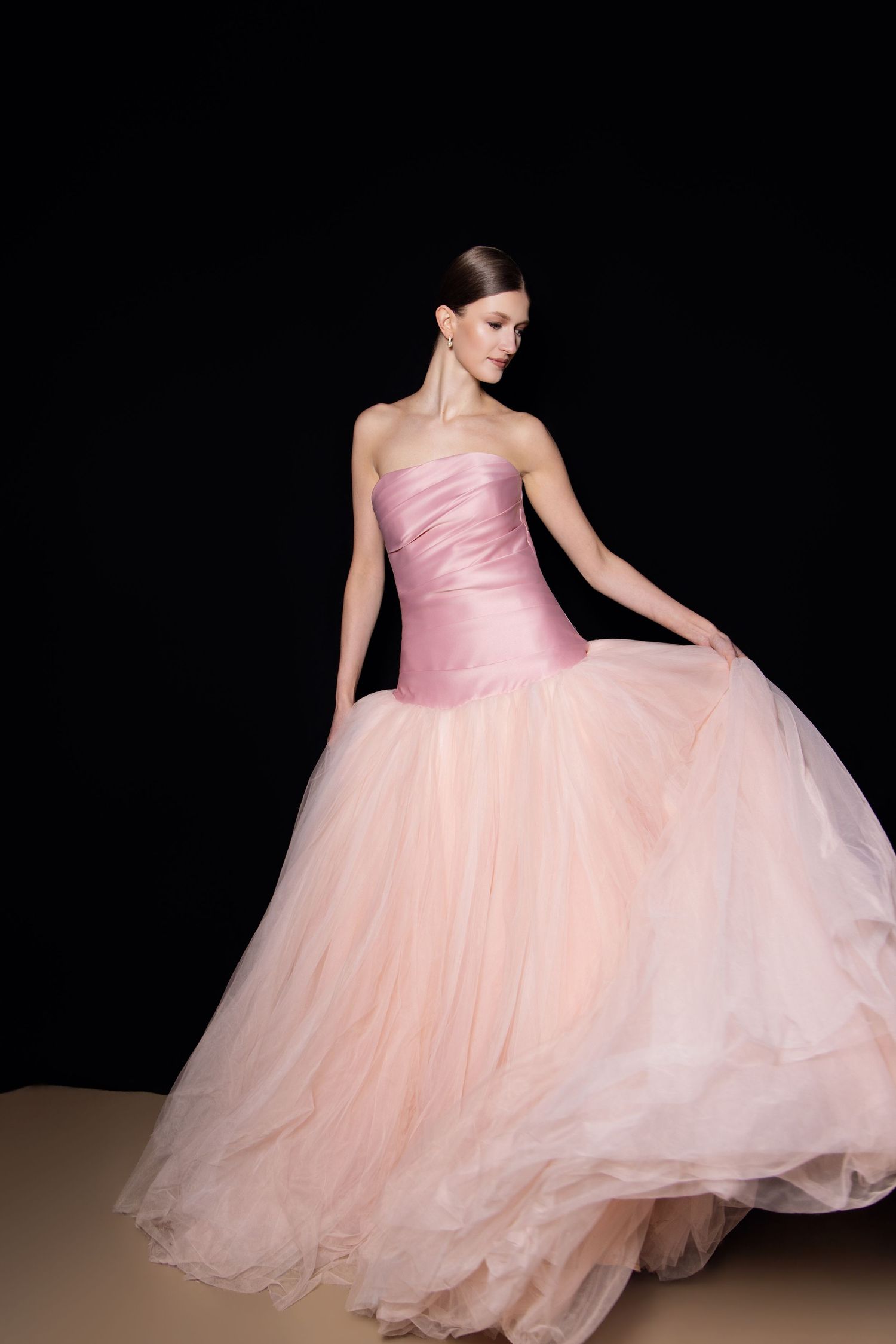 A ballet dancer in a flowing pink tulle gown performs graceful movements against a black background.